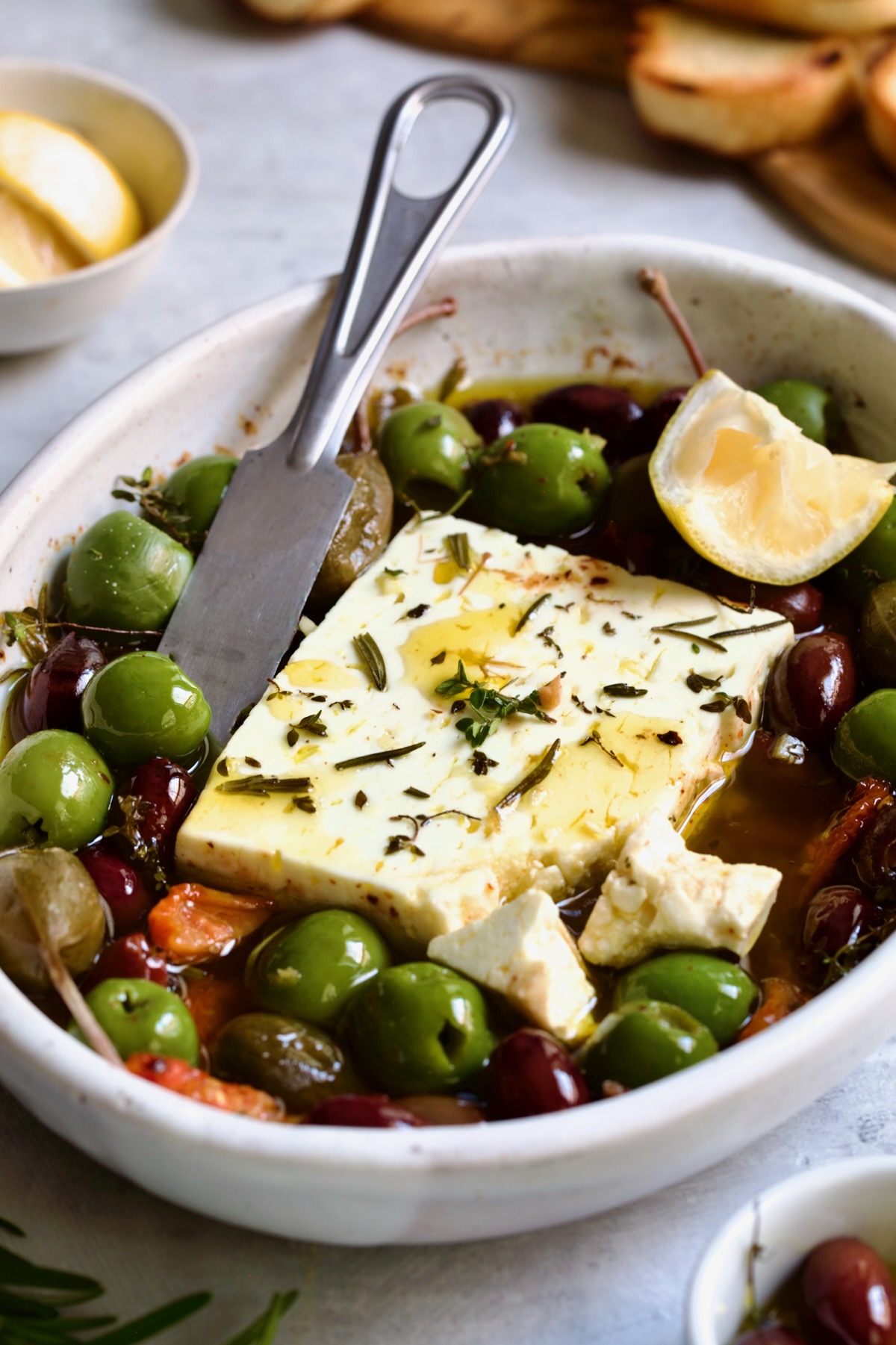 Baked Feta Cheese and Olives in white oval baking dish with serving knife.