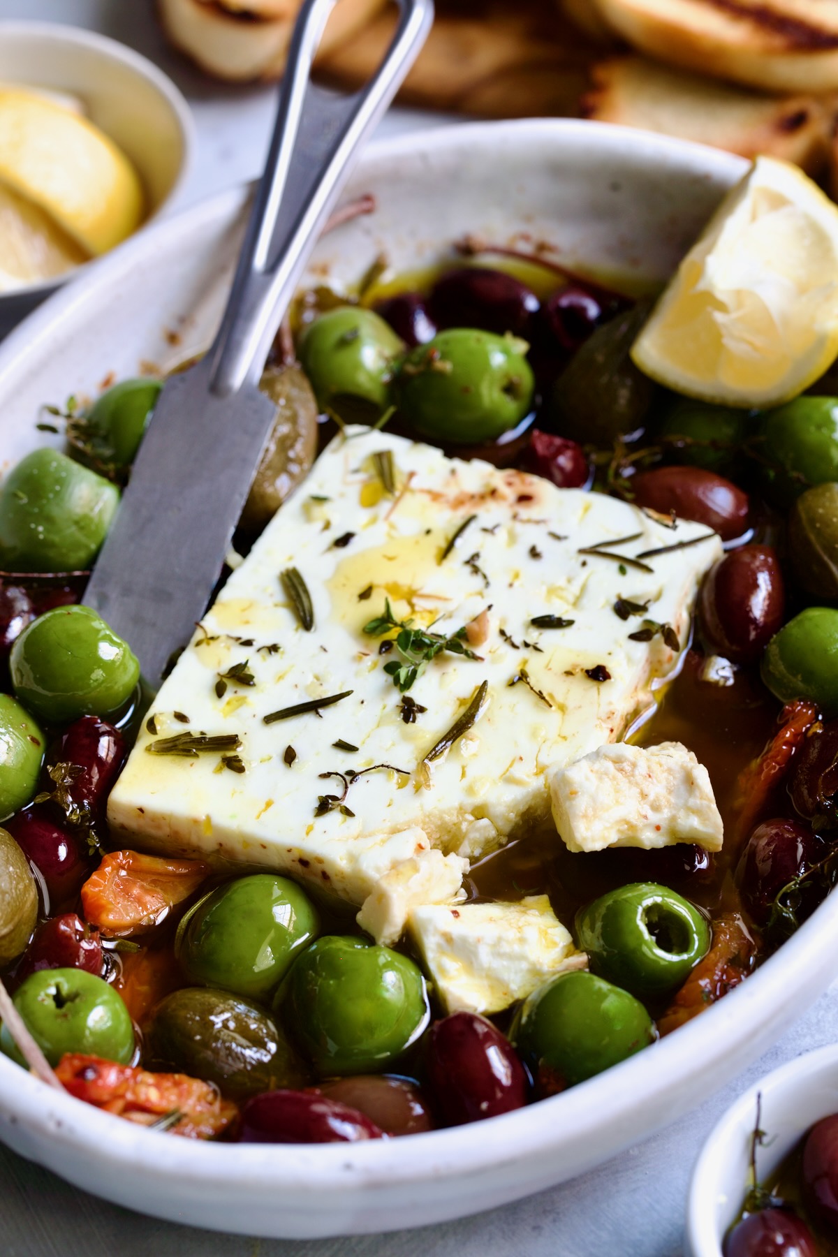 Baked Feta Cheese and Olives in white oval baking dish with serving knife.