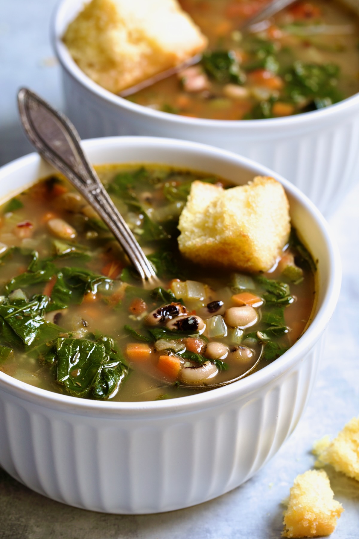 Two servings of Black-Eyed Pea Soup in white bowls with cornbread on top.