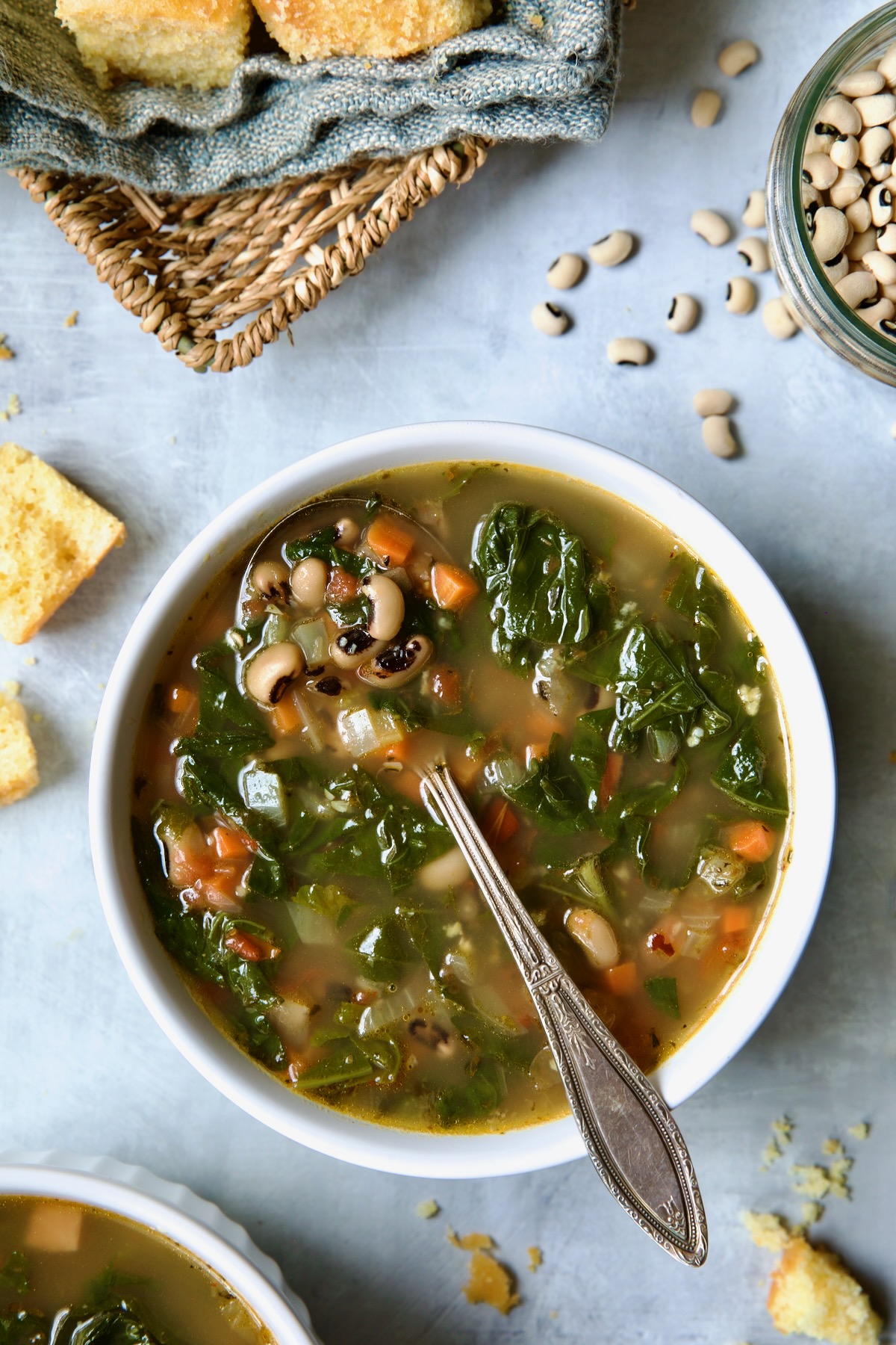 One serving of Black-Eyed Pea Soup in a white bowl with cornbread in a basket.
