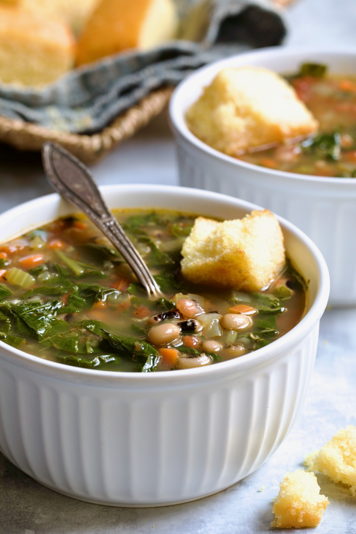Two servings of Black-Eyed Pea Soup in white bowls with cornbread on top.