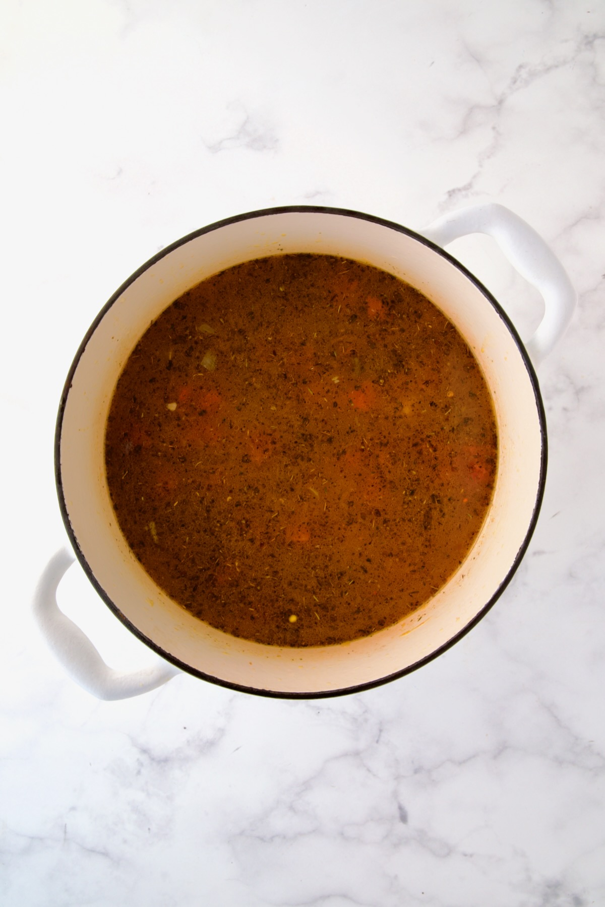 Broth and tomatoes added to cooked vegetables and spices in white Dutch oven.
