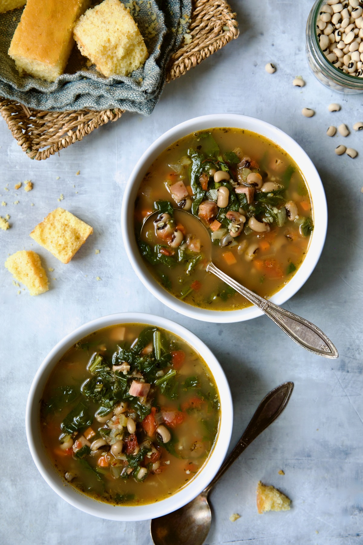 Two servings of Black-Eyed Pea Soup in white bowls with cornbread in a basket.