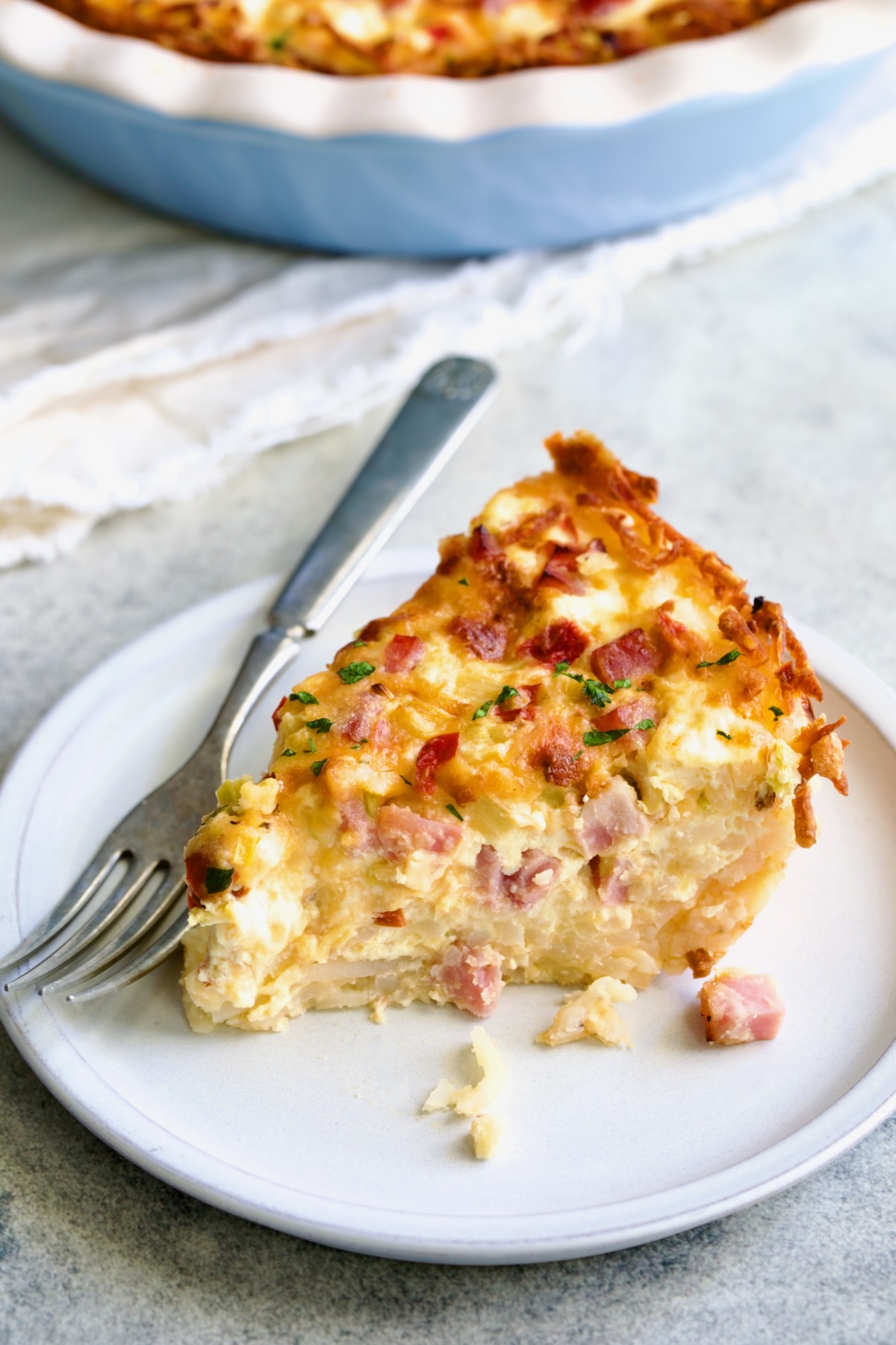 Piece of Quiche with Hash Brown Potato Crust on small white plate with fork.