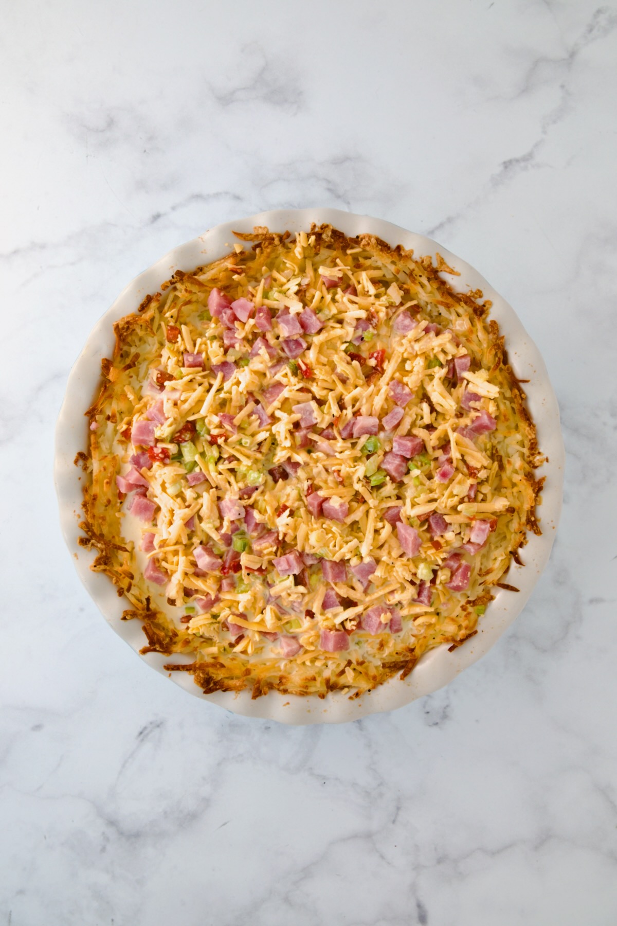 Custard poured over the cheese, ham and vegetables in white pie pan.