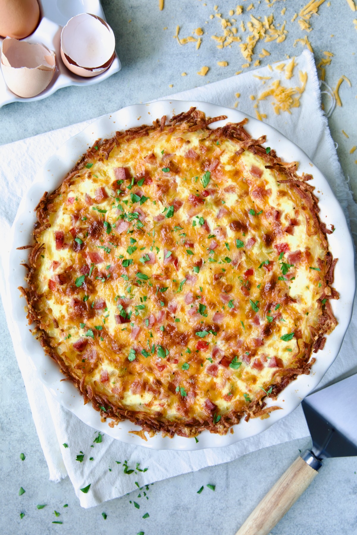 Whole baked Quiche with Hash Brown Potato Crust om white pie pan.