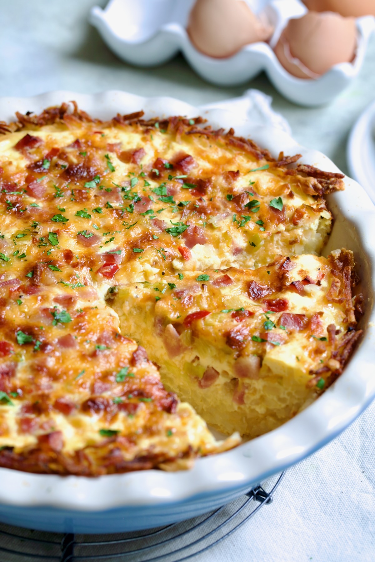 Quiche with Hash Brown Potato Crust in white pie pan with a wedge cut.