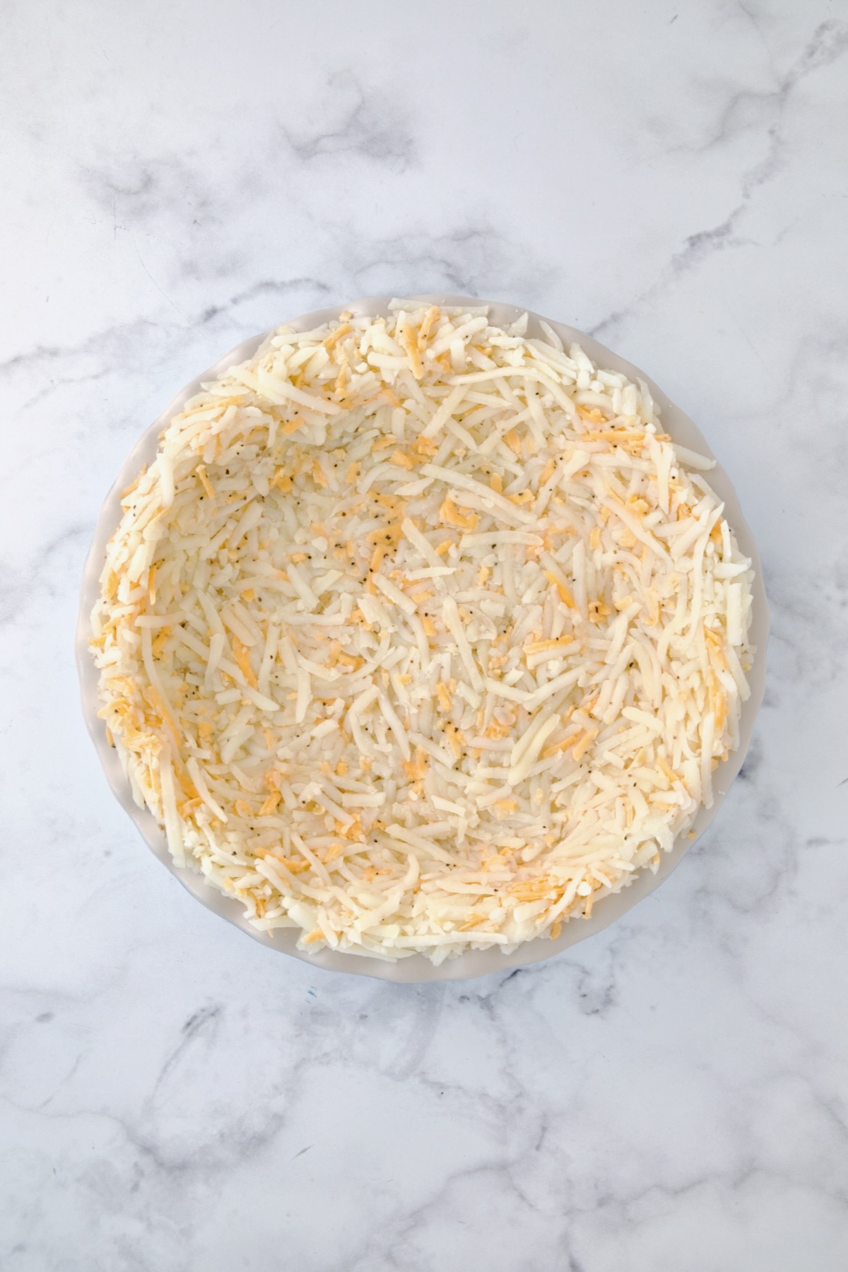 Unbaked hash brown potato crust in white pie pan.