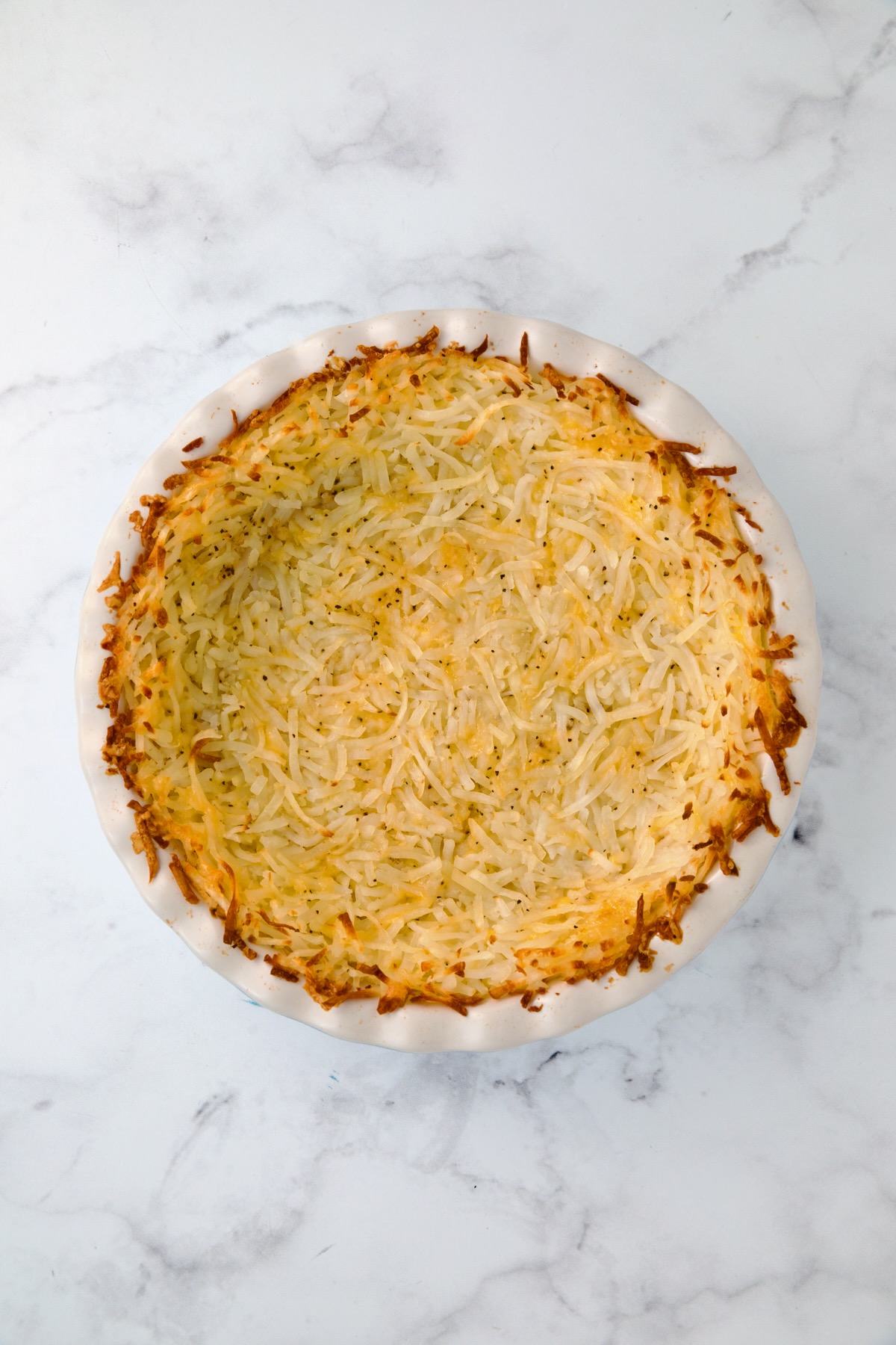 Baked hash brown potato crust in white pie pan.