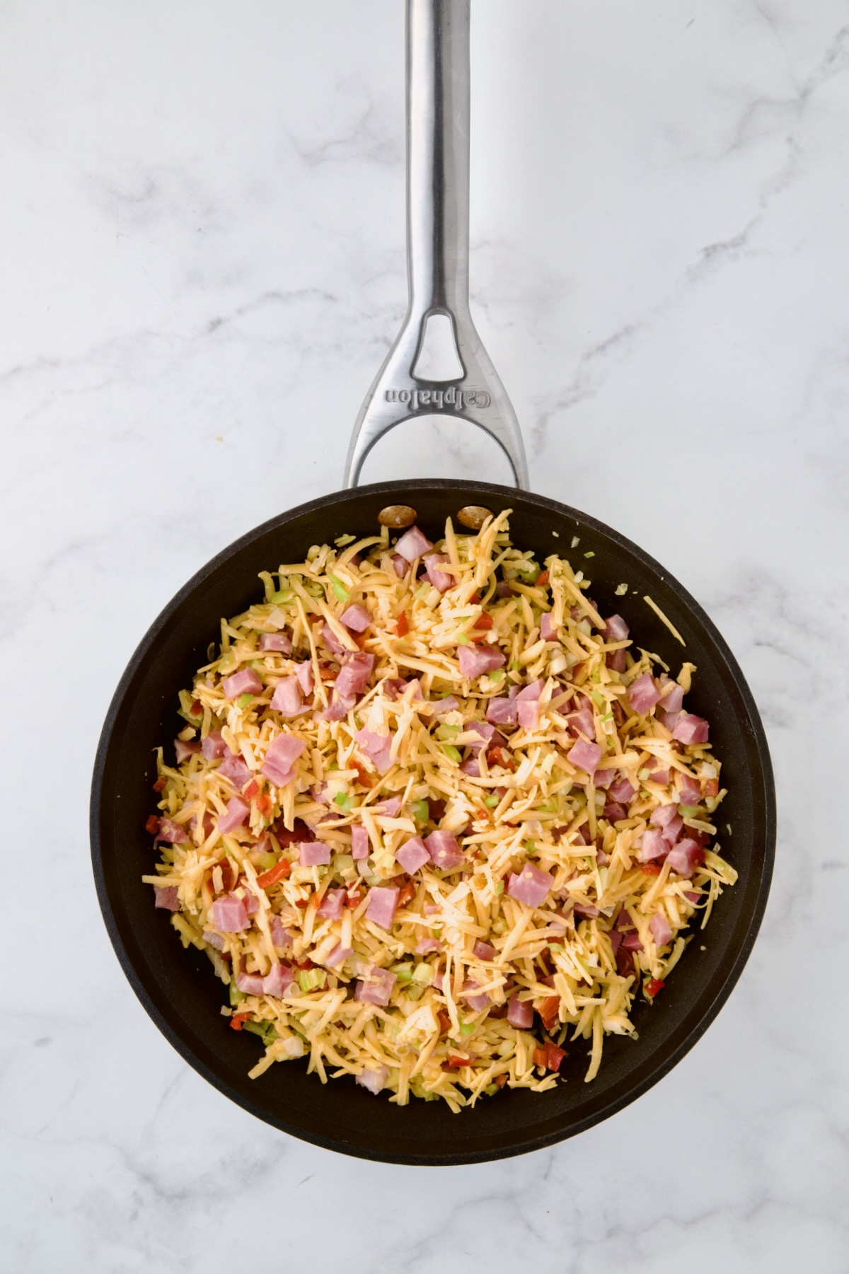 Cheese and ham added to cooked scallion and red bell pepper in nonstick skillet.