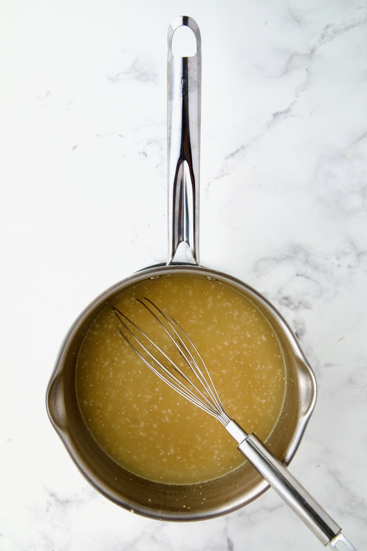 Polenta added to chicken broth in stainless steel saucepan with wire whisk.