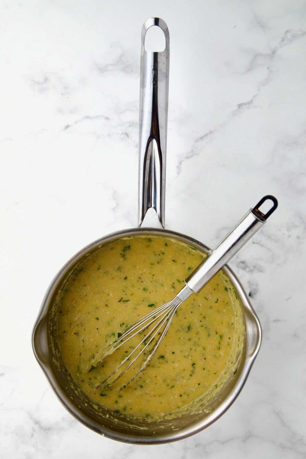 Polenta in stainless steel saucepan with wire whisk.