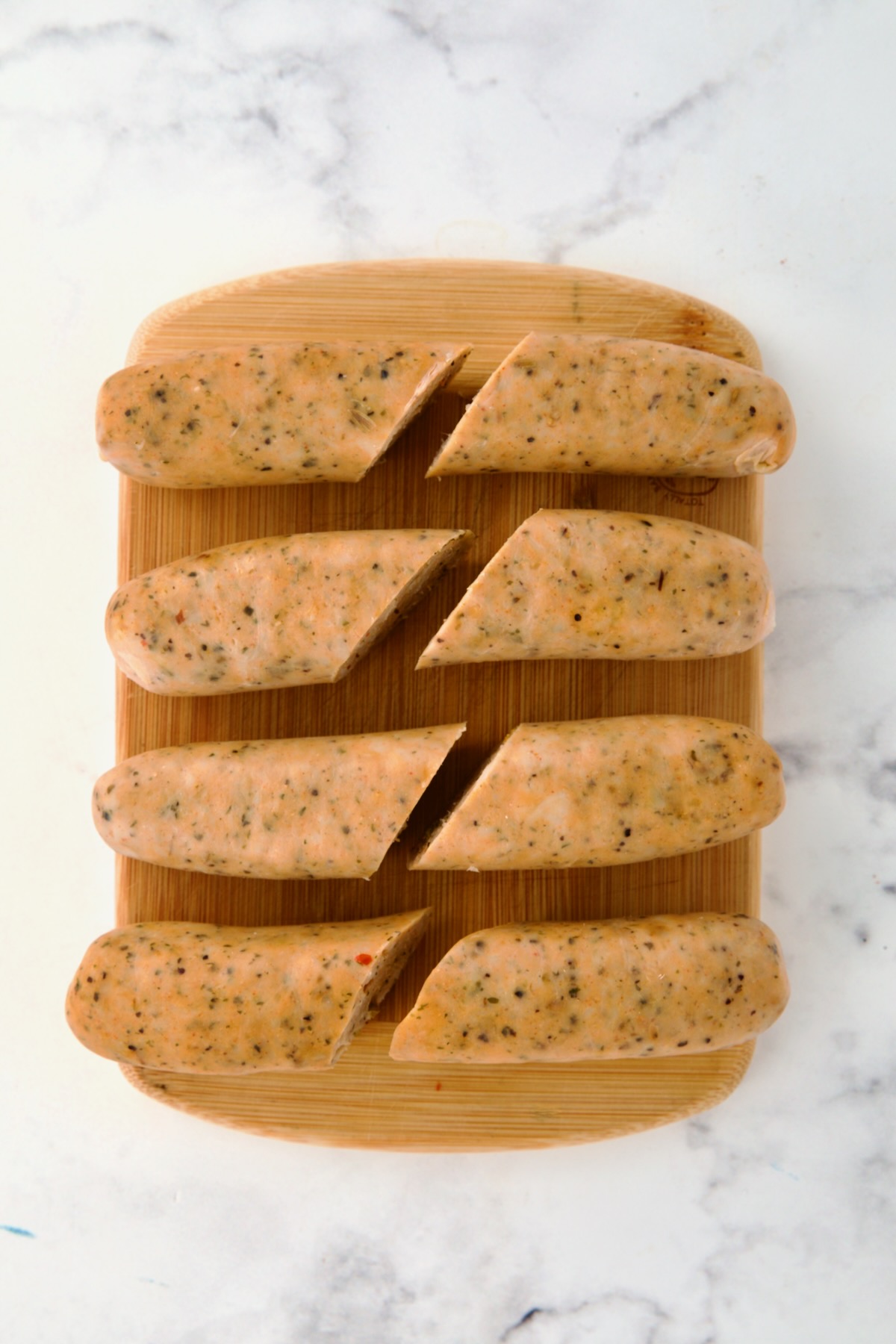 Four links of chicken sausage on bamboo cutting board cut in half for eight pieces.