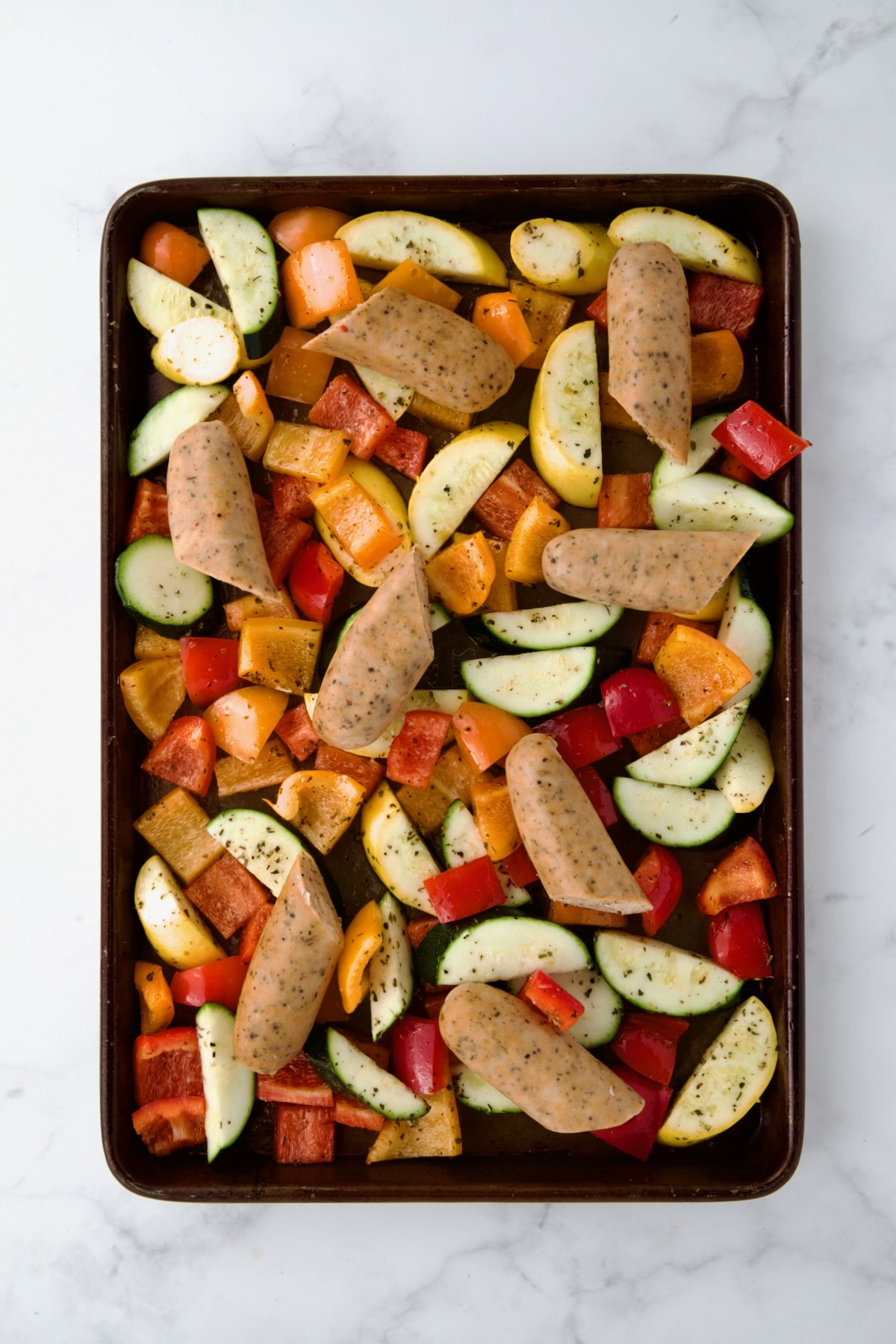 Uncooked chicken sausage and vegetables on rimmed sheet pan.