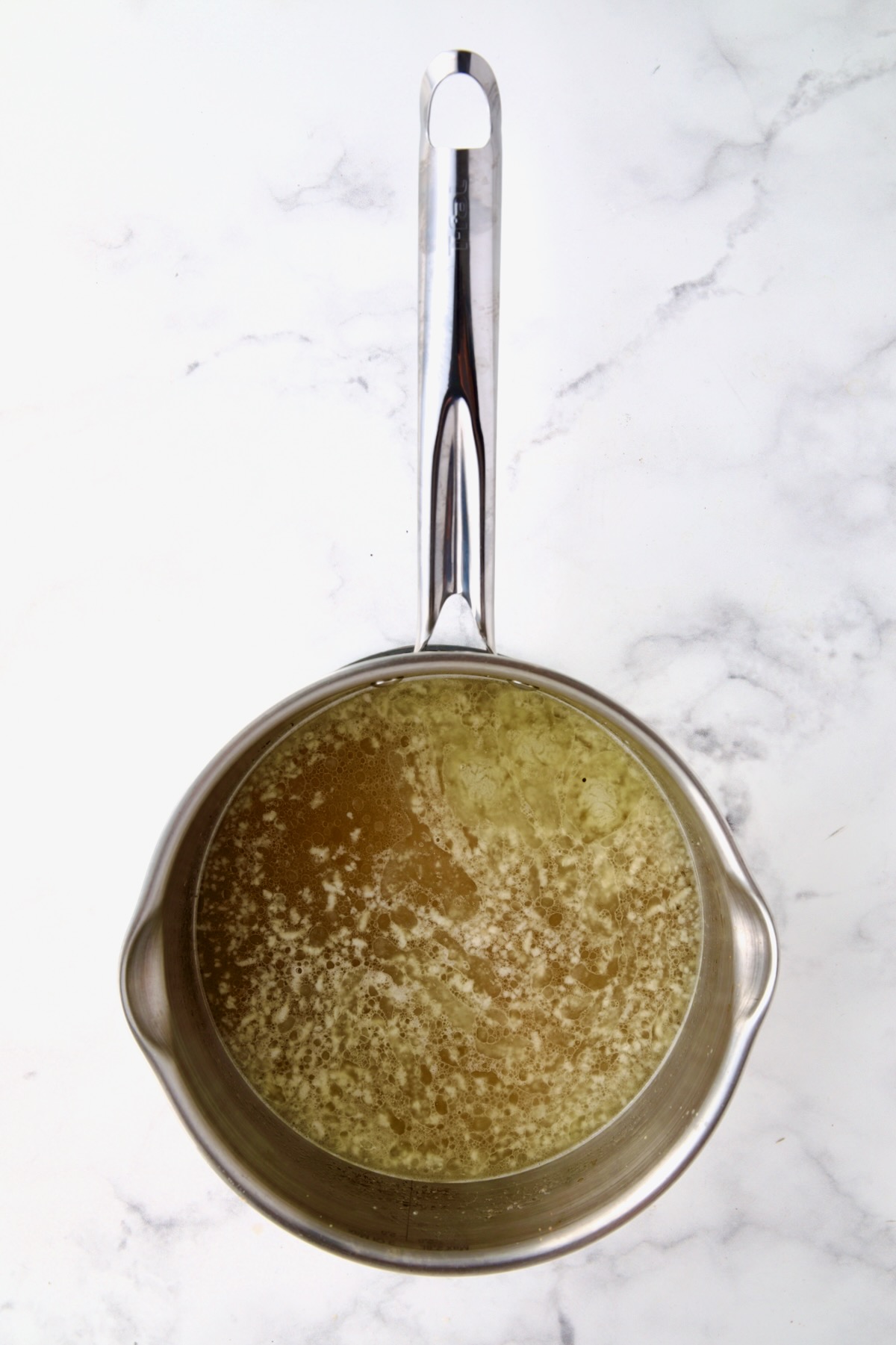 Boiling chicken broth and butter in stainless steel saucepan.