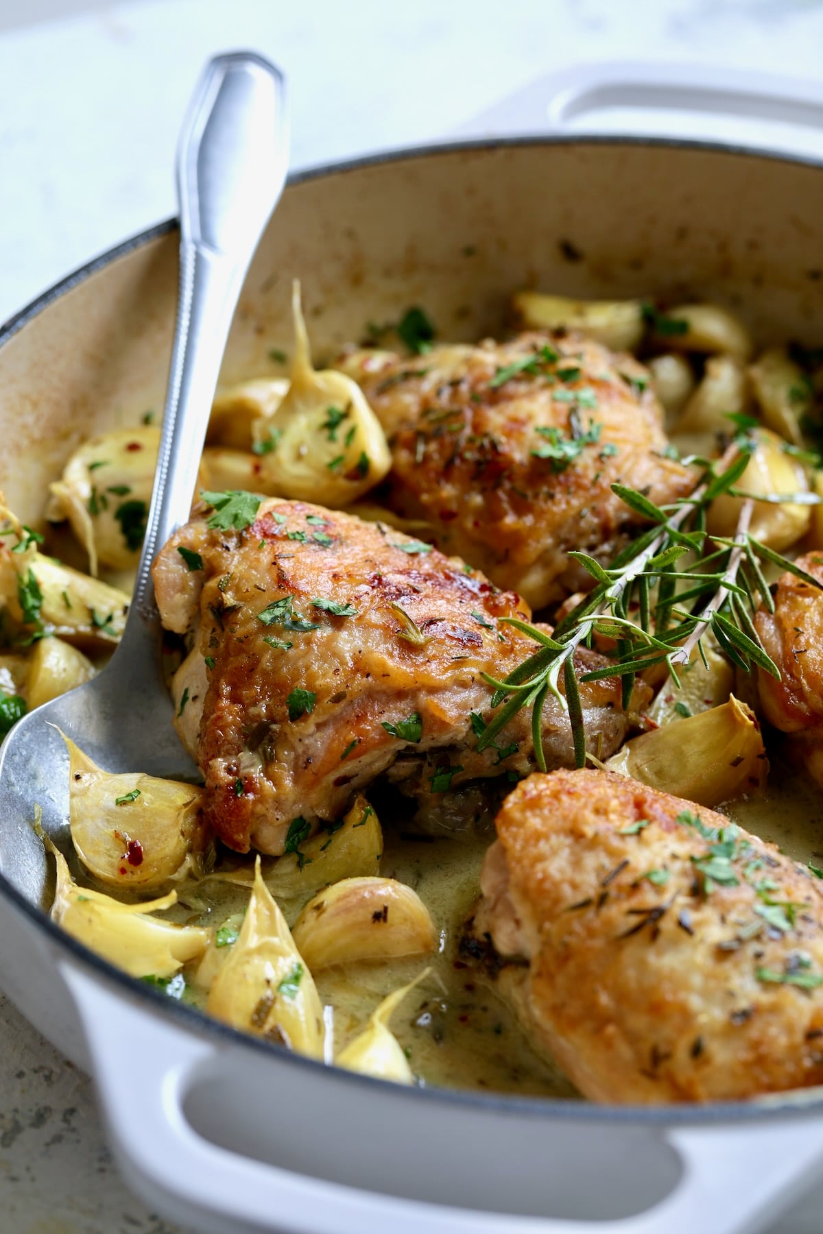 Four servings of 40 Clove Garlic Chicken in white enamel cast iron skillet.