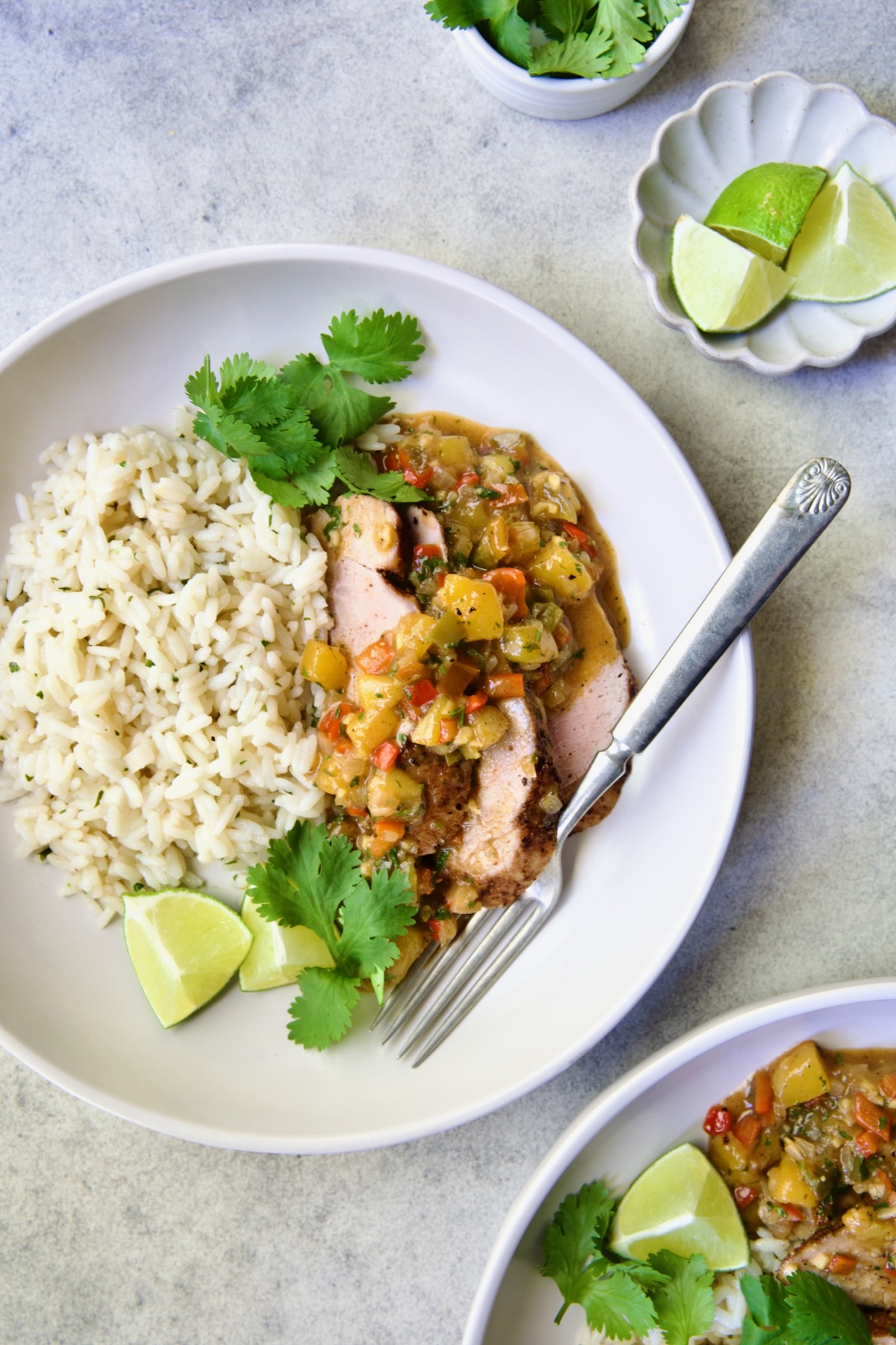 One serving of sliced and sauced Caribbean Pork Tenderloin in white dinner bowl garnished with cilantro and lime wedges.