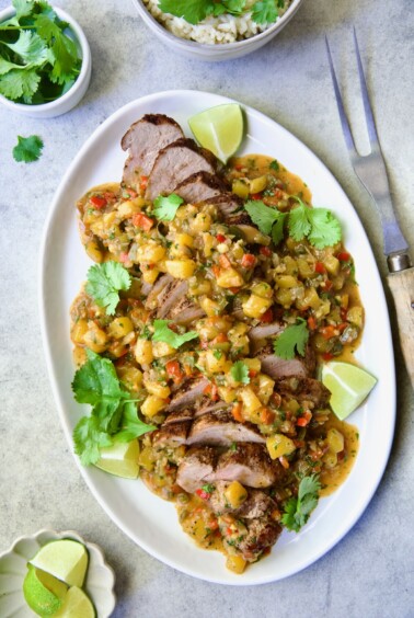 Sliced and sauced Caribbean Pork Tenderloin on white oval platter garnished with cilantro and lime wedges.