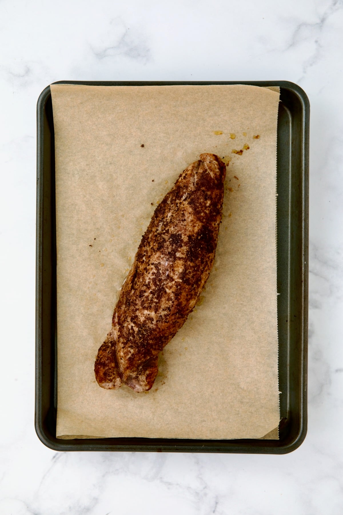 Baked pork tenderloin on brown parchment paper on rimmed baking sheet.