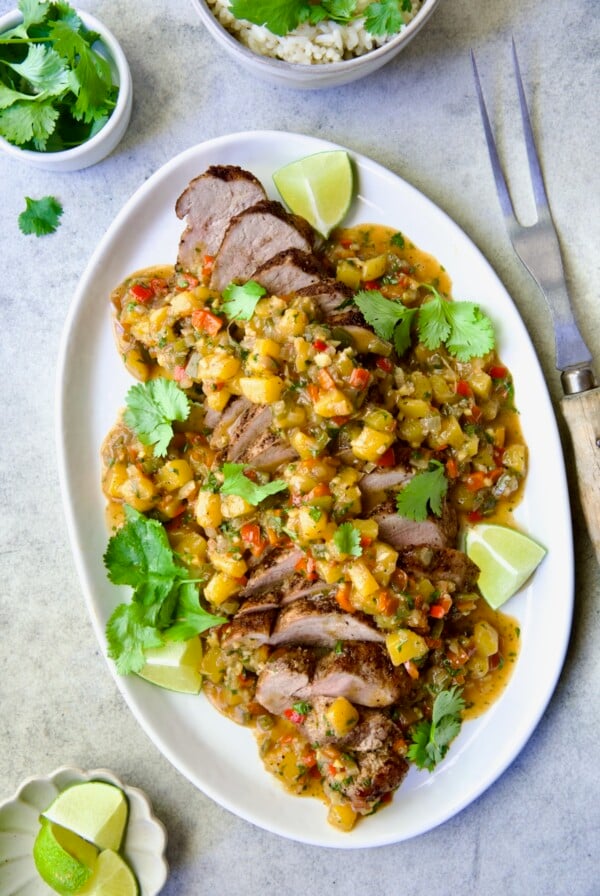 Sliced and sauced Caribbean Pork Tenderloin on white oval platter garnished with cilantro and lime wedges.