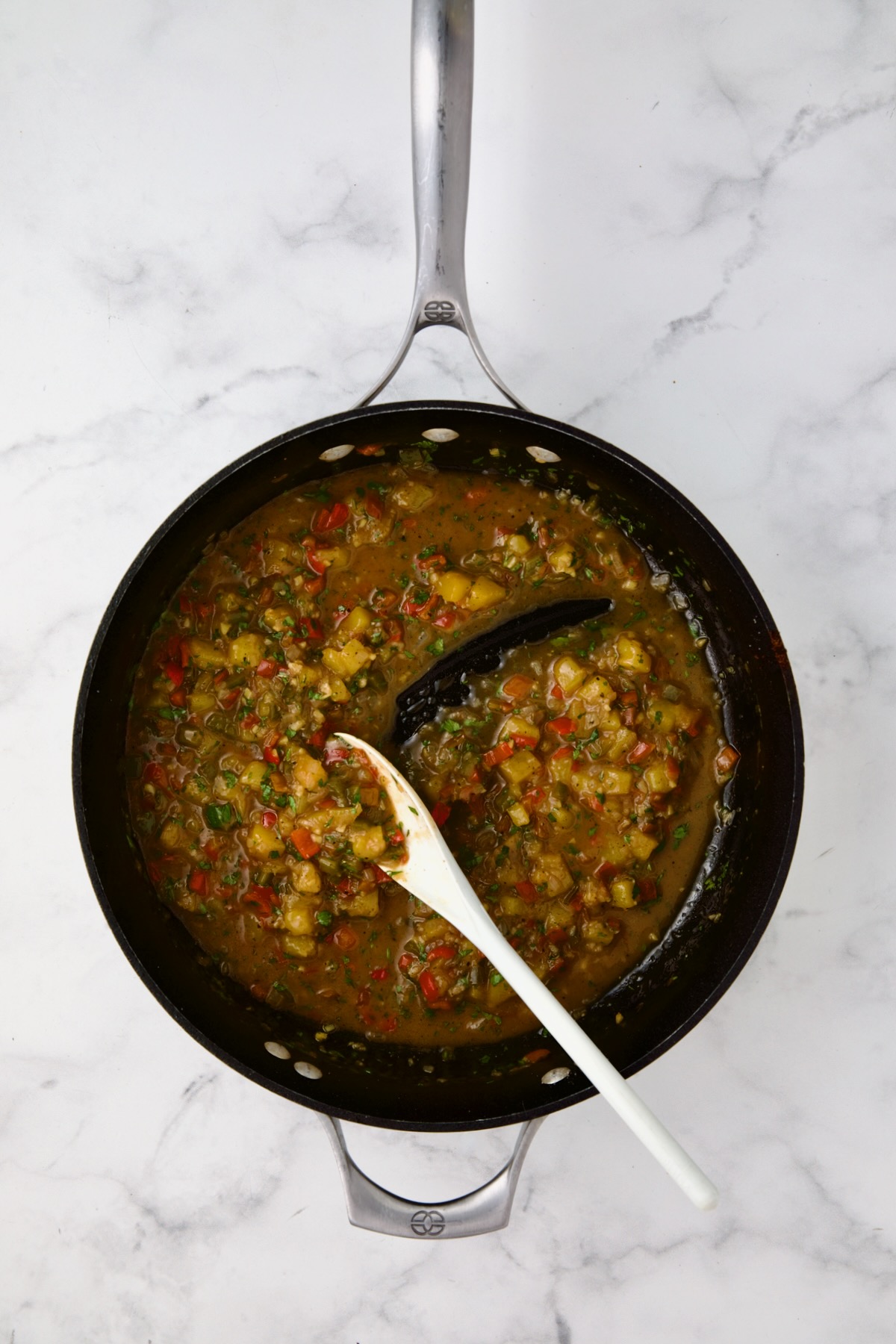 Finished mango sauce in nonstick skillet being stirred with white mixing spoon.