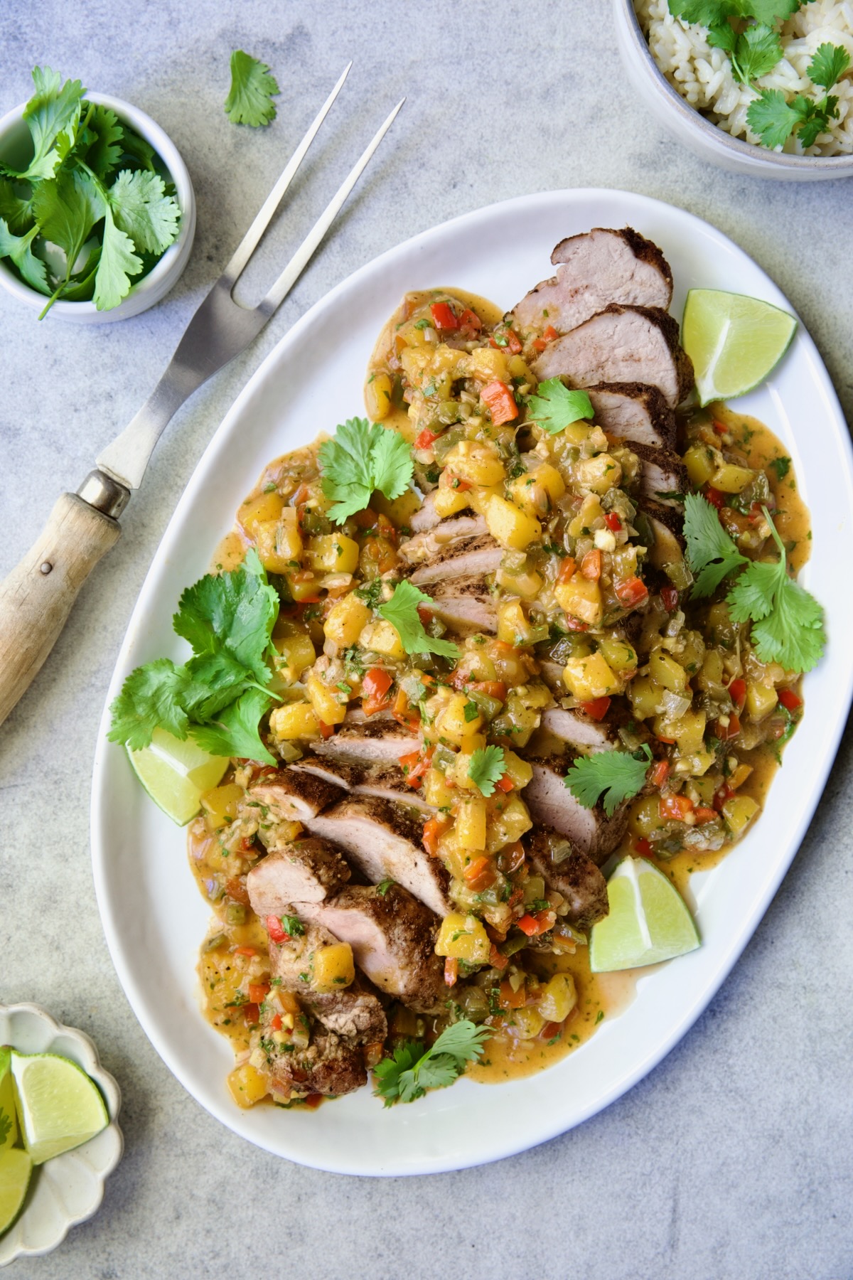 Sliced and sauced Caribbean Pork Tenderloin on white oval platter garnished with cilantro and lime wedges.