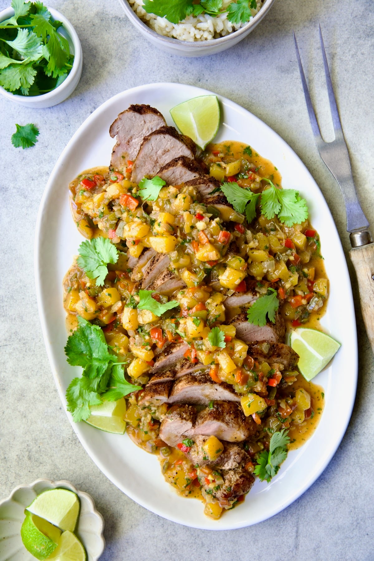 Sliced and sauced Caribbean Pork Tenderloin on white oval platter garnished with cilantro and lime wedges.