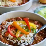 One serving of Southwestern Red Beans and Rice in a white bowl garnished with colorful sauteed bell peppers.