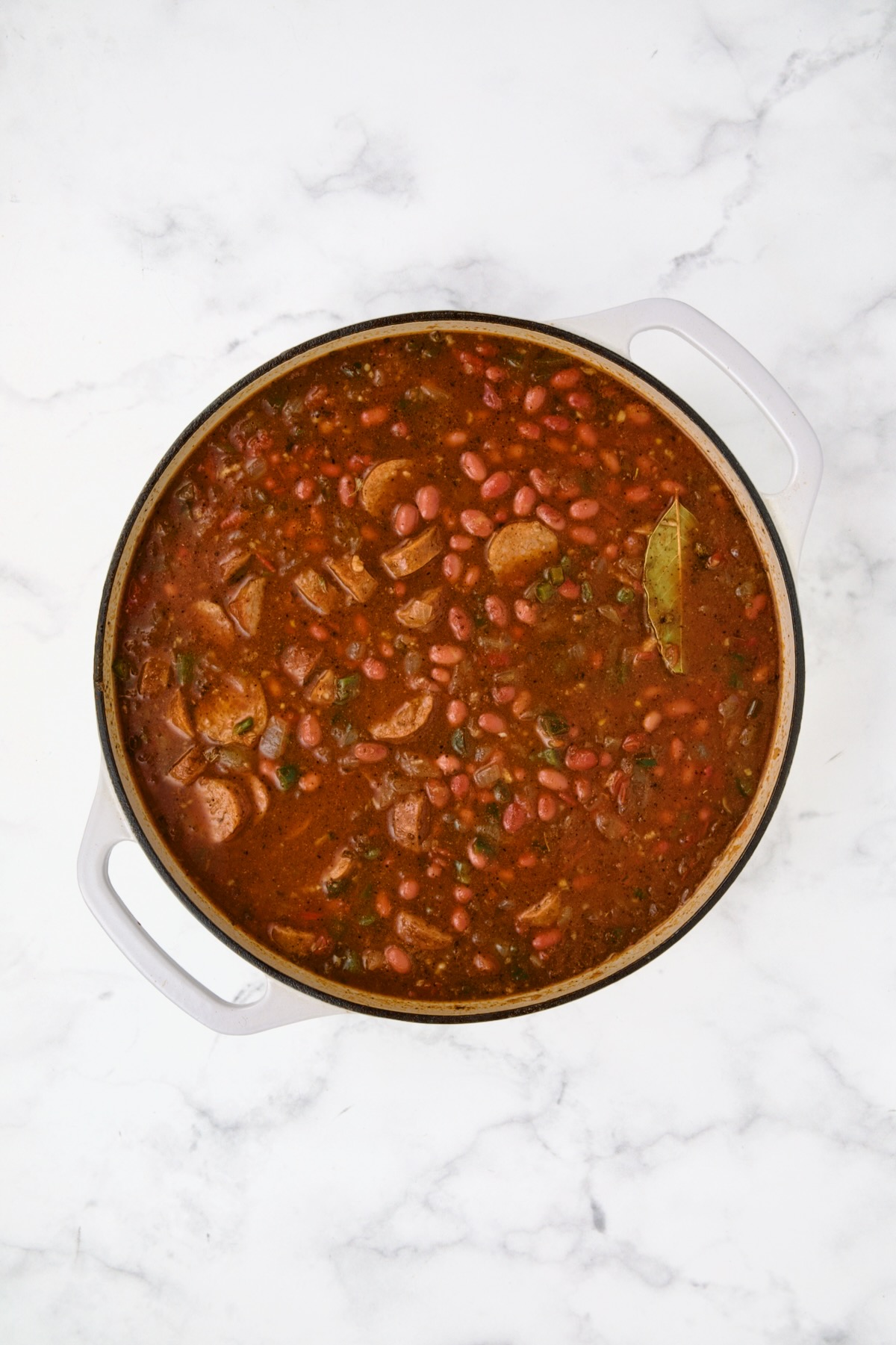 All ingredients for beans in white enamel cast iron skillet ready to be simmered.