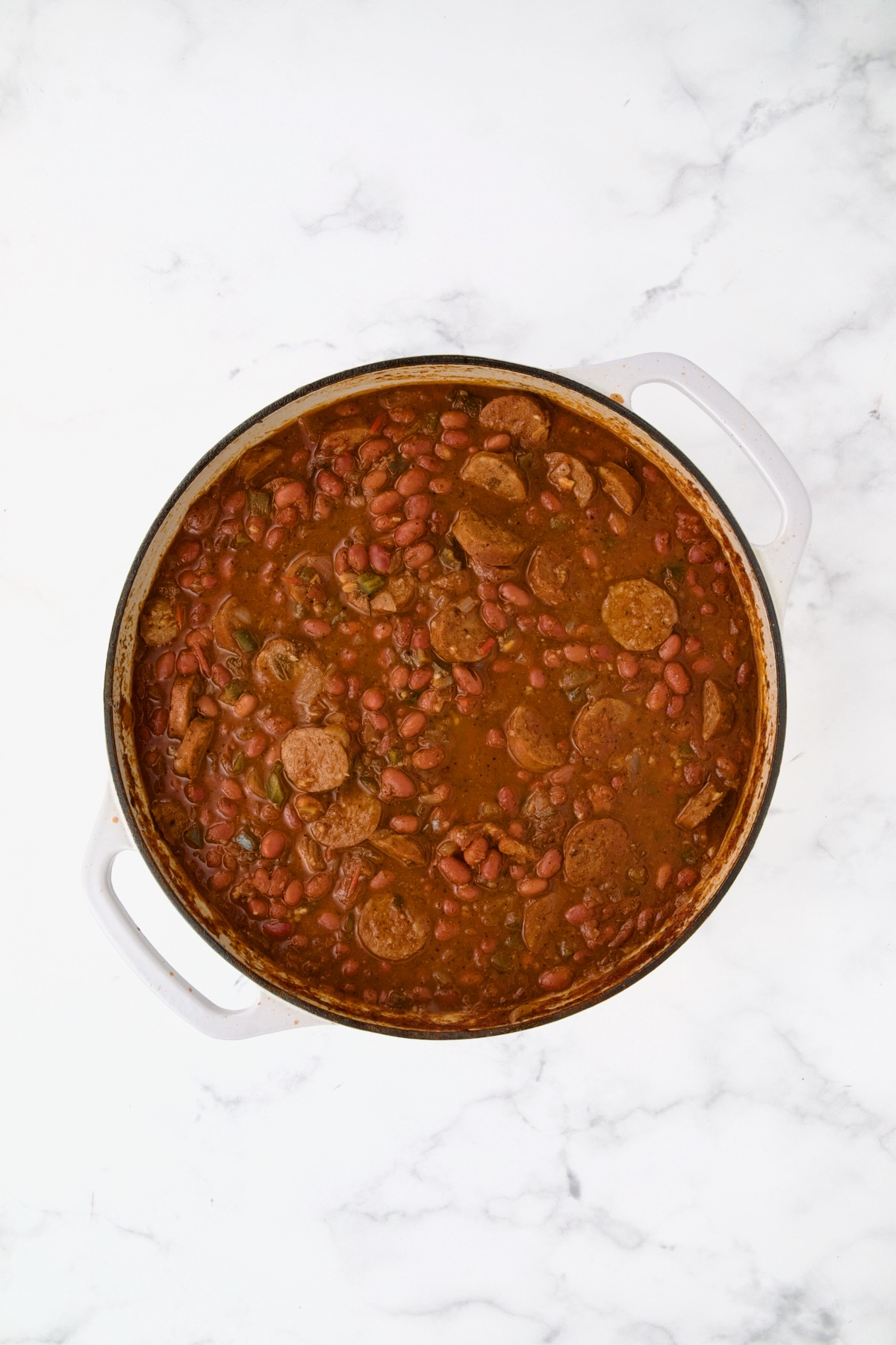Cooked red beans and chorizo sausage in white enamel cast iron skillet.
