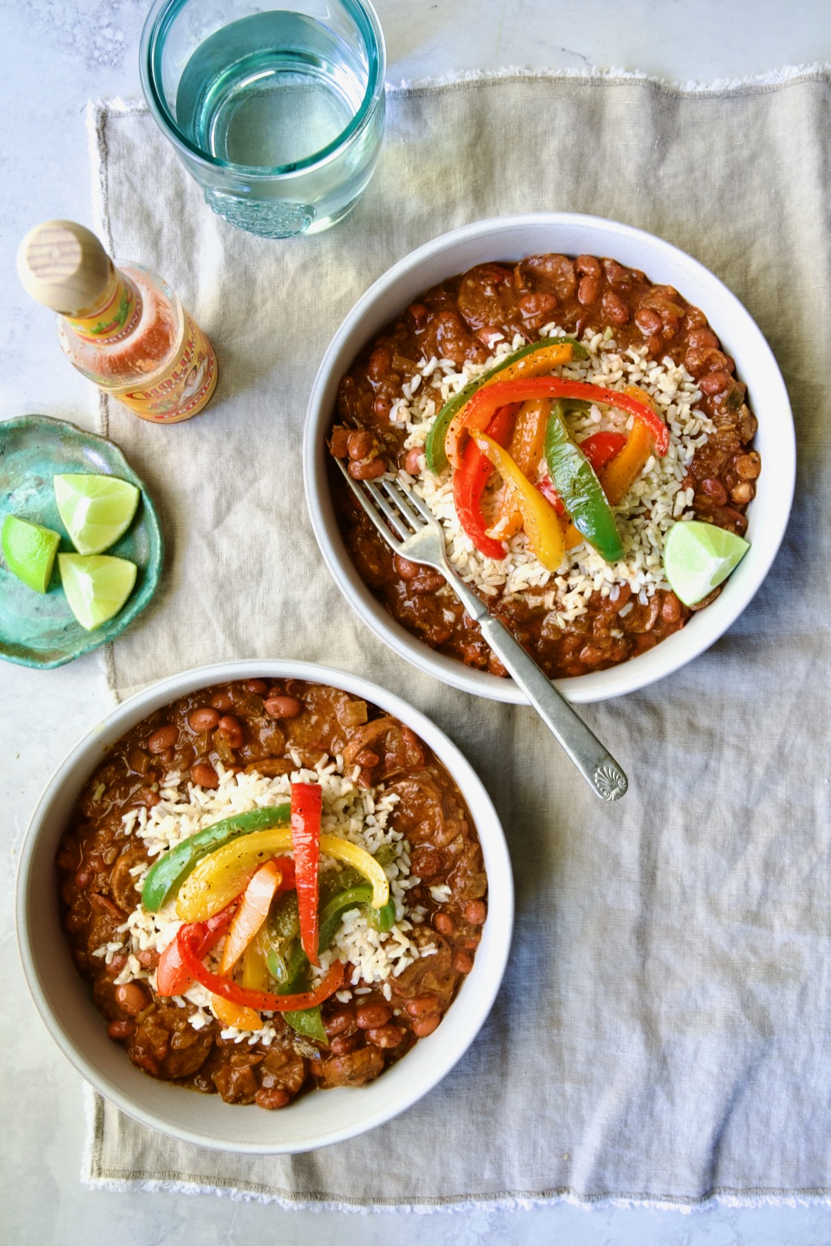 Two servings of Southwestern Red Beans and Rice in white bowls garnished with colorful sauteed bell peppers.