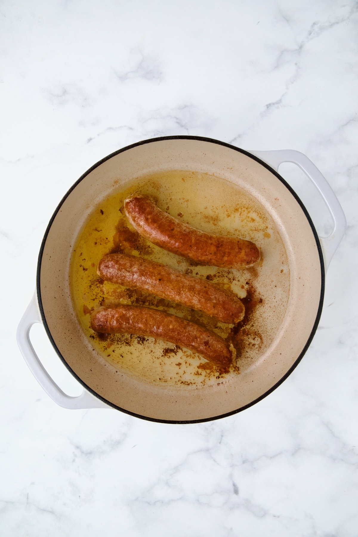 Three links of cooked chorizo sausage in white enamel cast iron skillet.