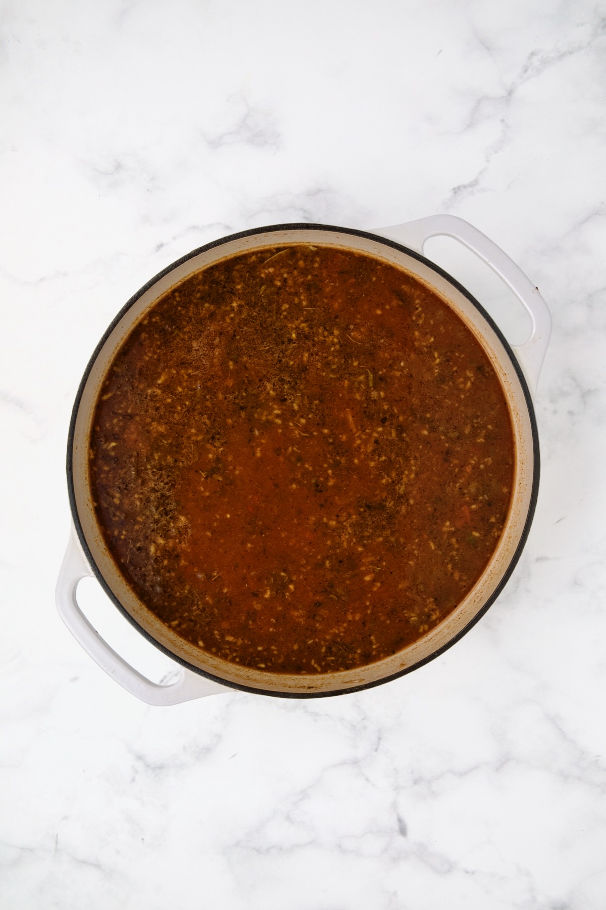Tomato sauce and broth added to onion, peppers and spices in white enamel cast iron skillet.