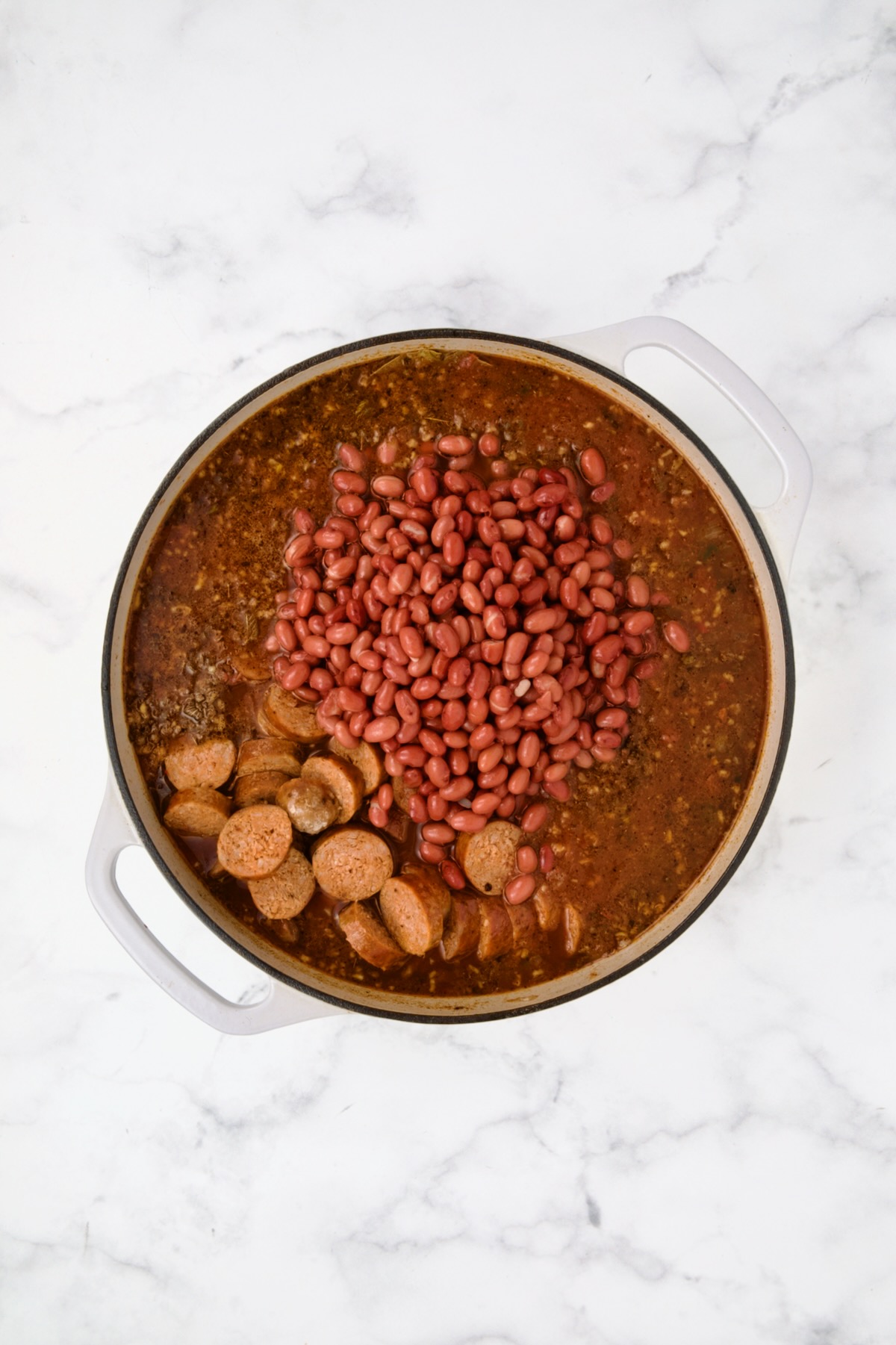 Beans and chorizo added to sauce, broth and spices in white enamel cast iron skillet.