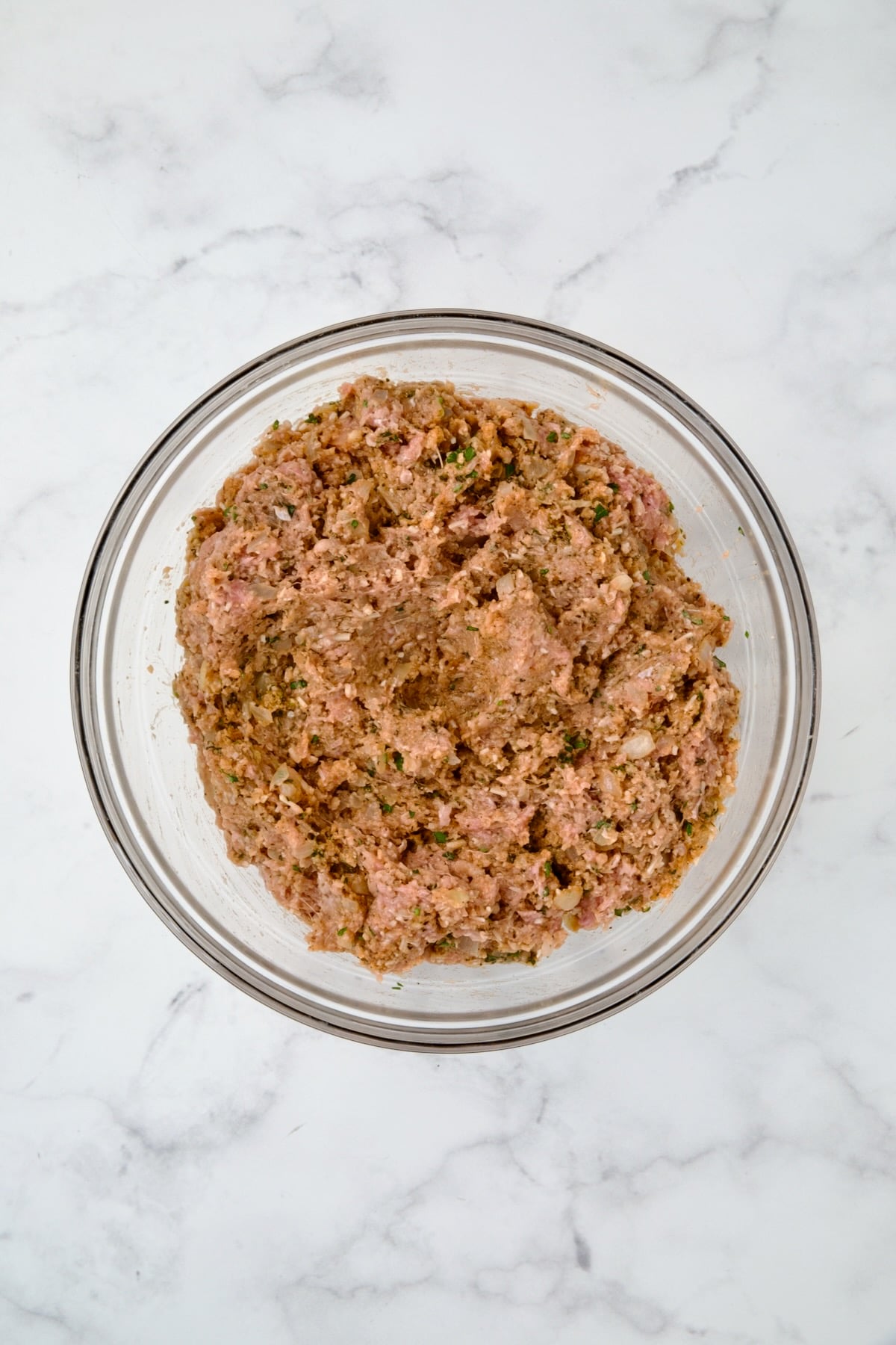 Ingredients for meatloaf in glass bowl after the meat is added.