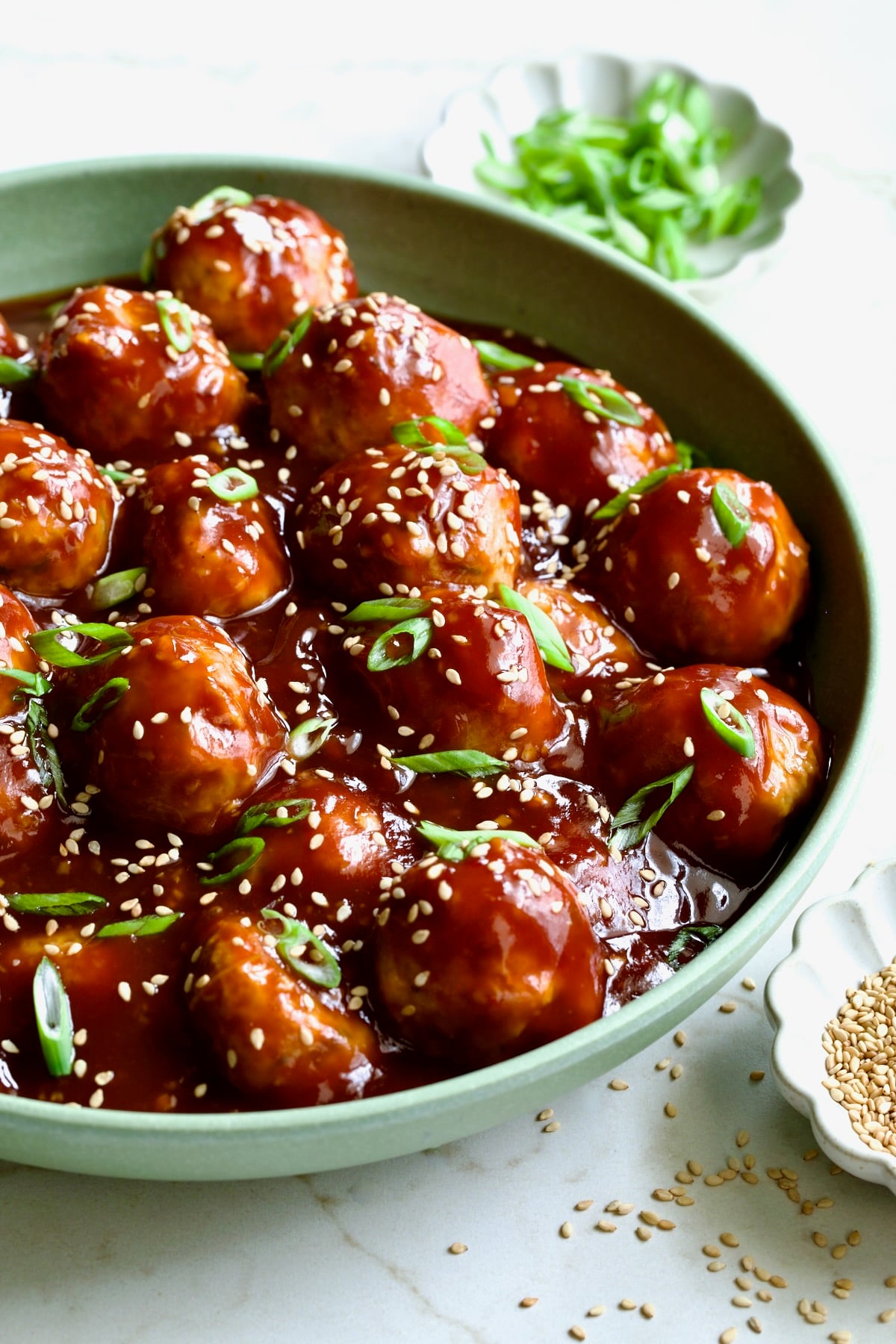 Asian Chicken Meatballs in round green bowl garnished with sesame seeds and scalllions.