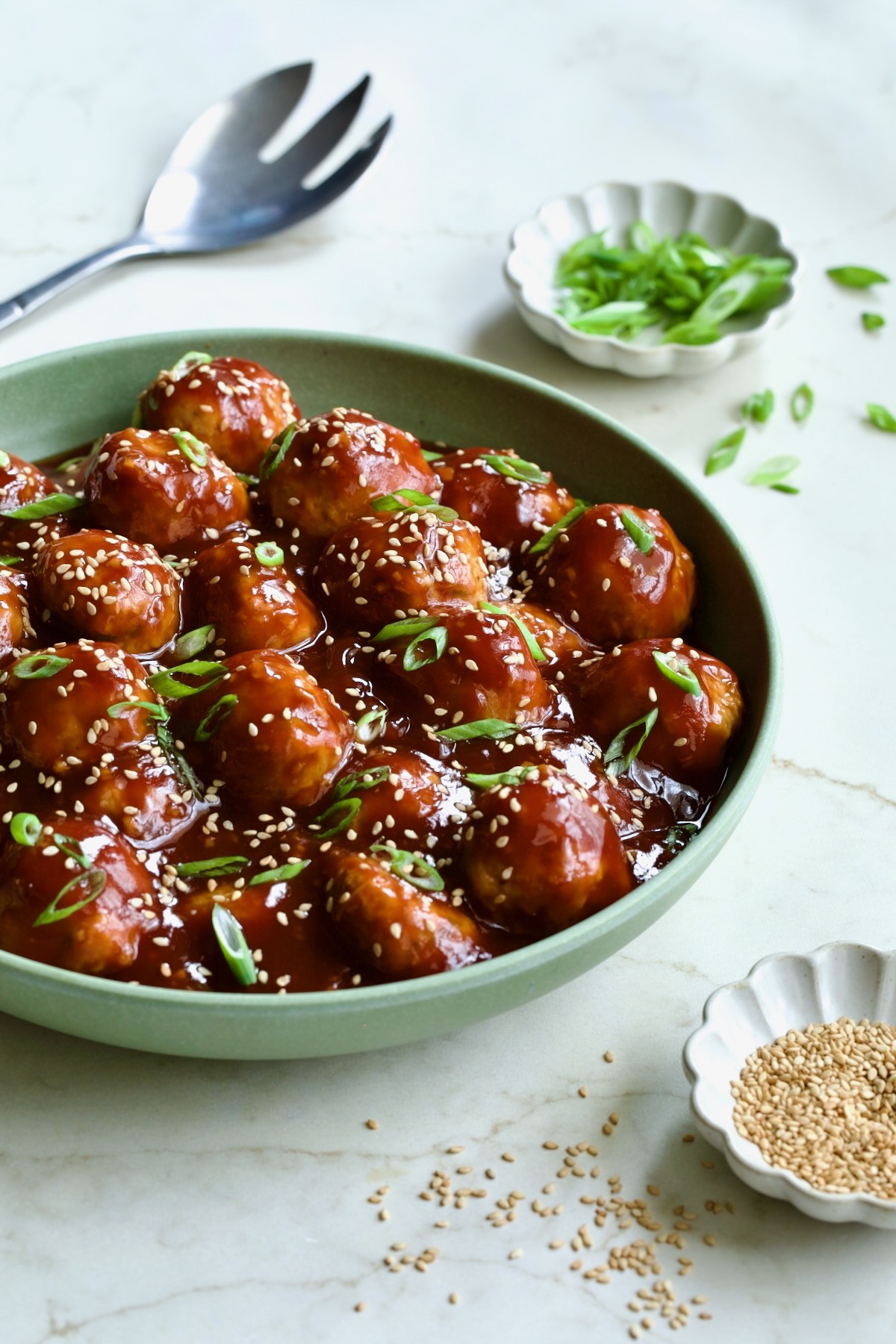 Asian Chicken Meatballs in round green bowl garnished with sesame seeds and scalllions.