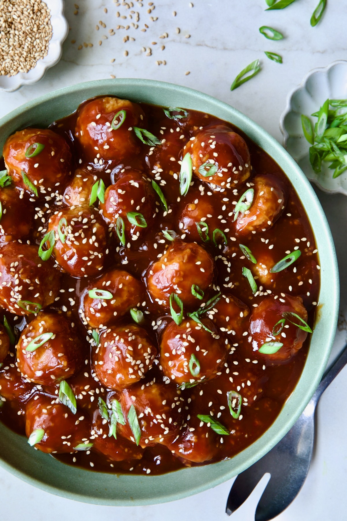 Asian Chicken Meatballs in round green bowl garnished with sesame seeds and scalllions.