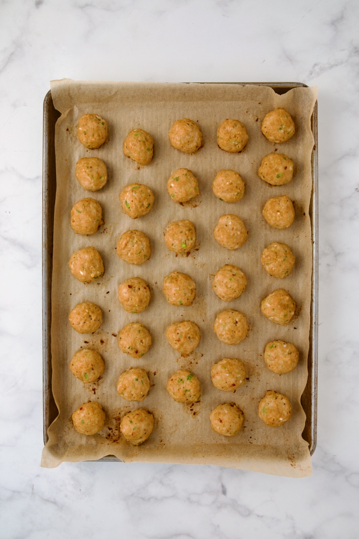 Cooked chicken meatballs on parchment paper-lined rimmed baking sheet.