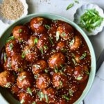 Asian Chicken Meatballs in round green bowl garnished with sesame seeds and scalllions.