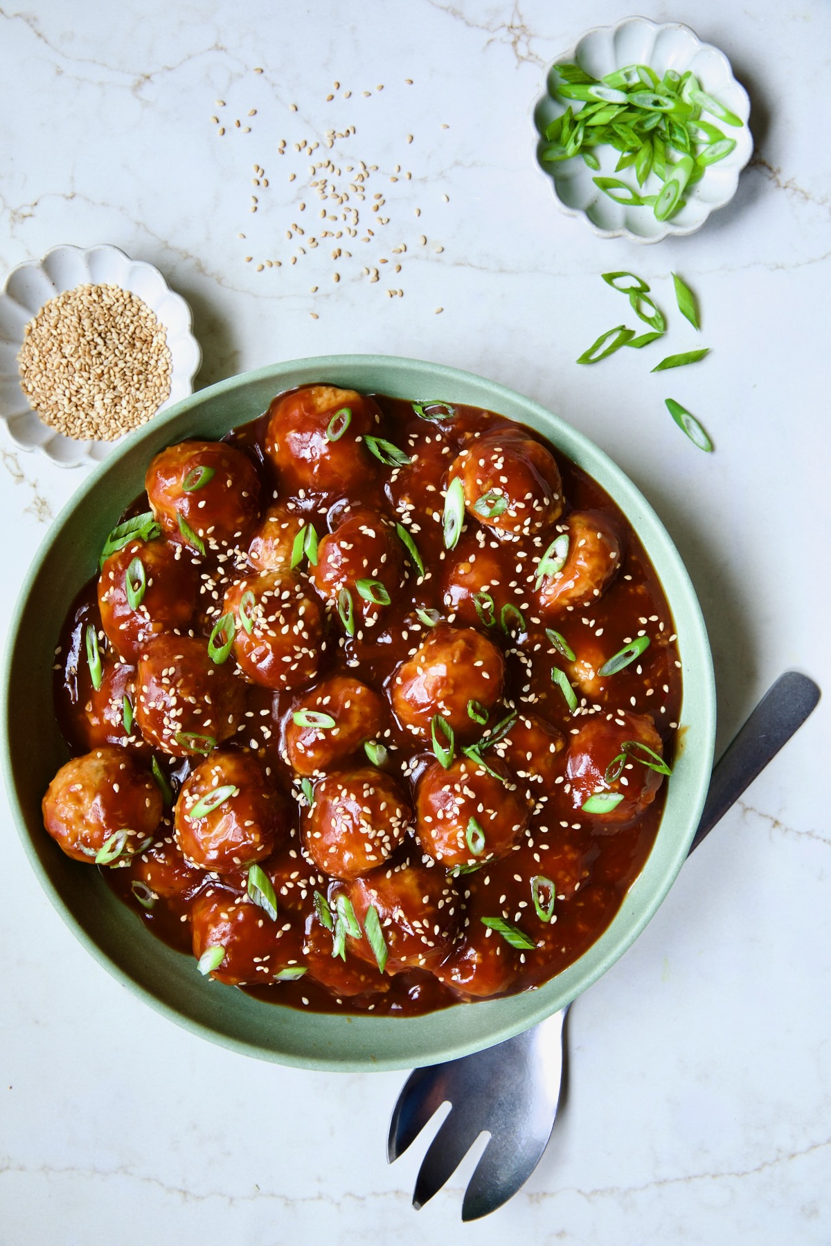 Asian Chicken Meatballs in round green bowl garnished with sesame seeds and scalllions.