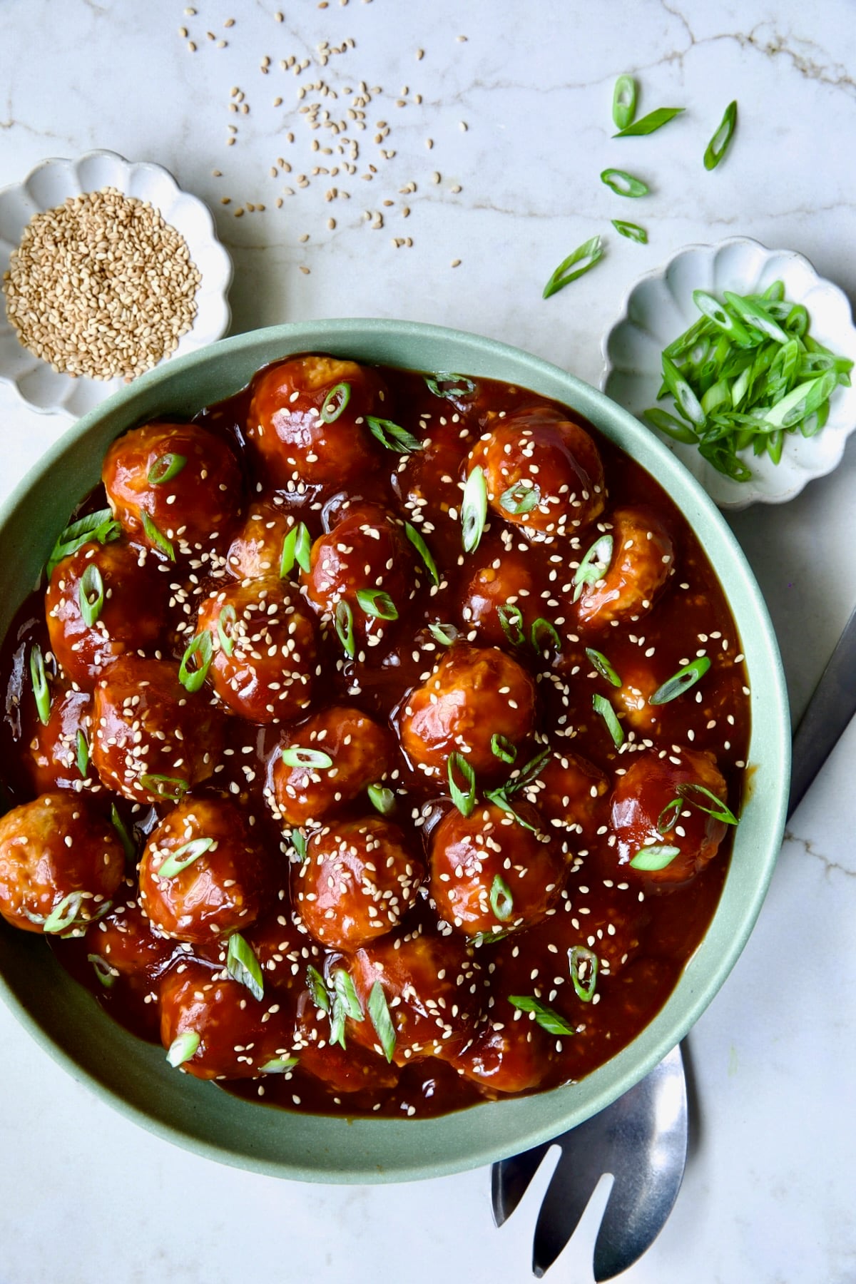 Asian Chicken Meatballs in round green bowl garnished with sesame seeds and scalllions.