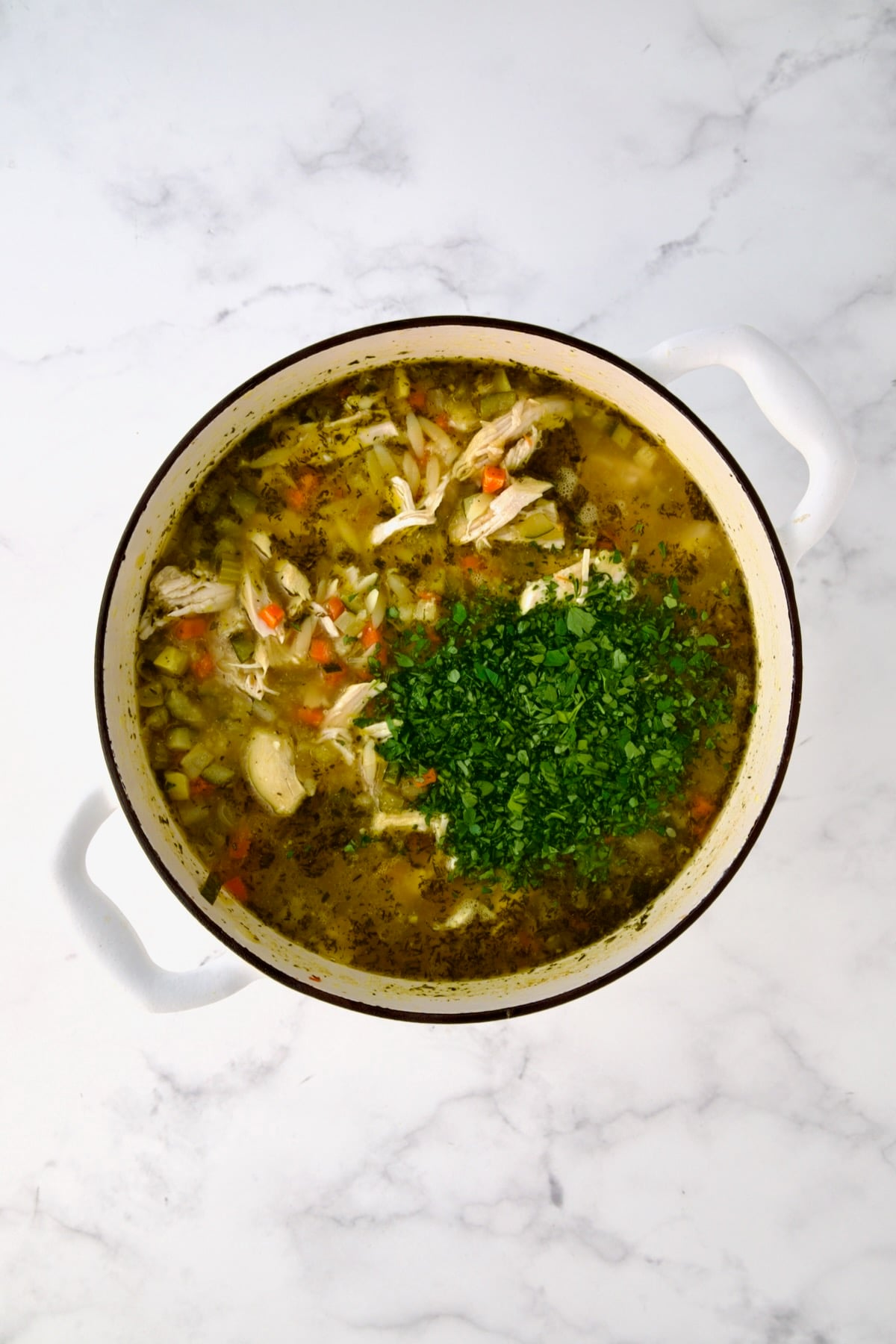 Chopped fresh parsley added to soup in white Dutch oven.