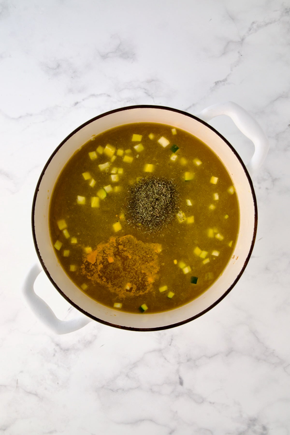 Chicken broth, thyme and turmeric added to vegetables in white Dutch oven.