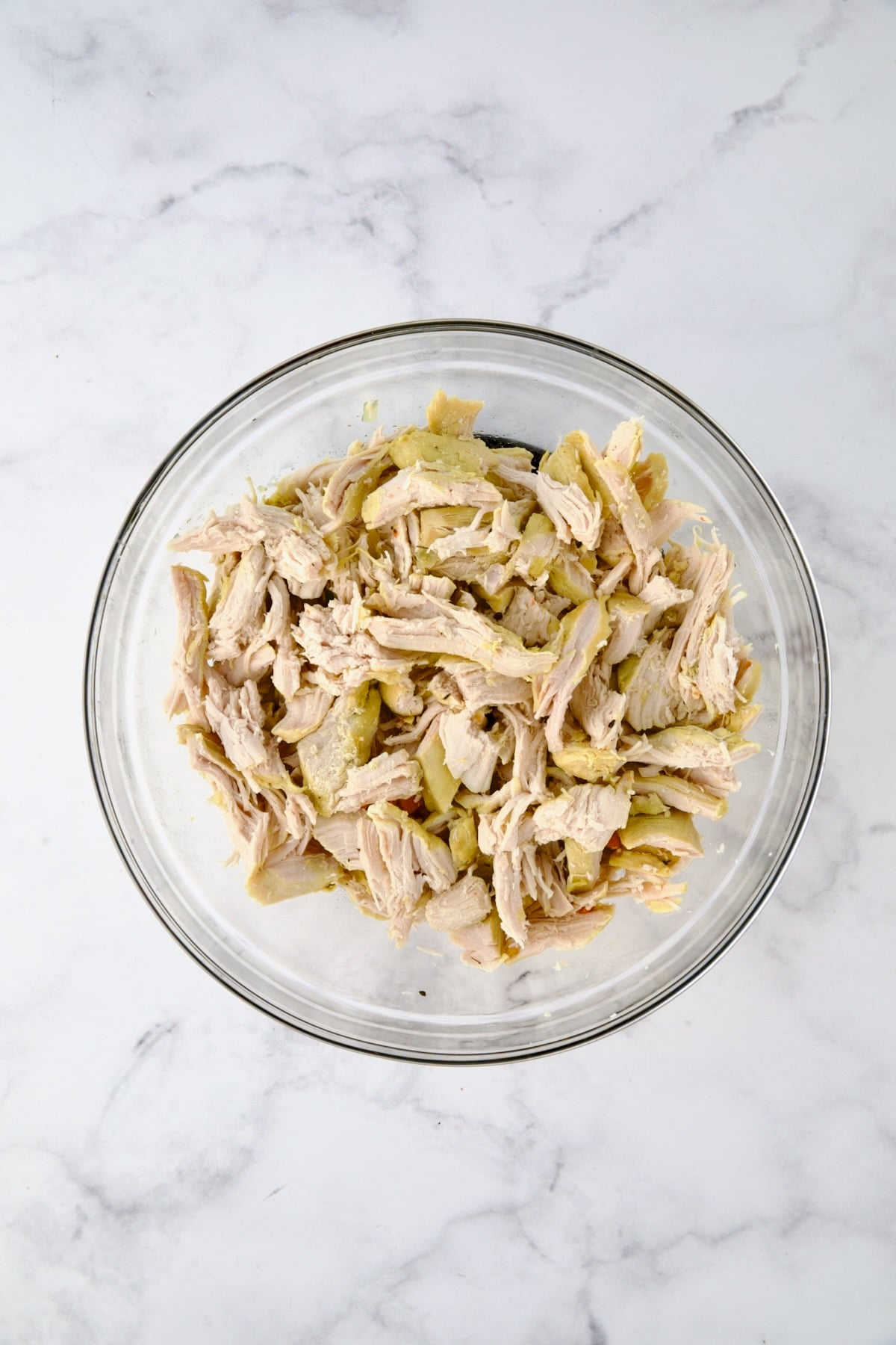 Cooked, shredded chicken in glass bowl.