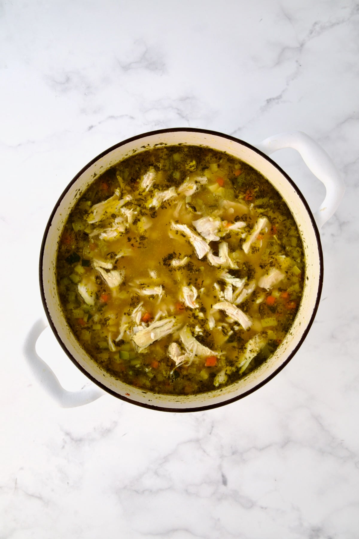 Chicken added to soup in white Dutch oven.