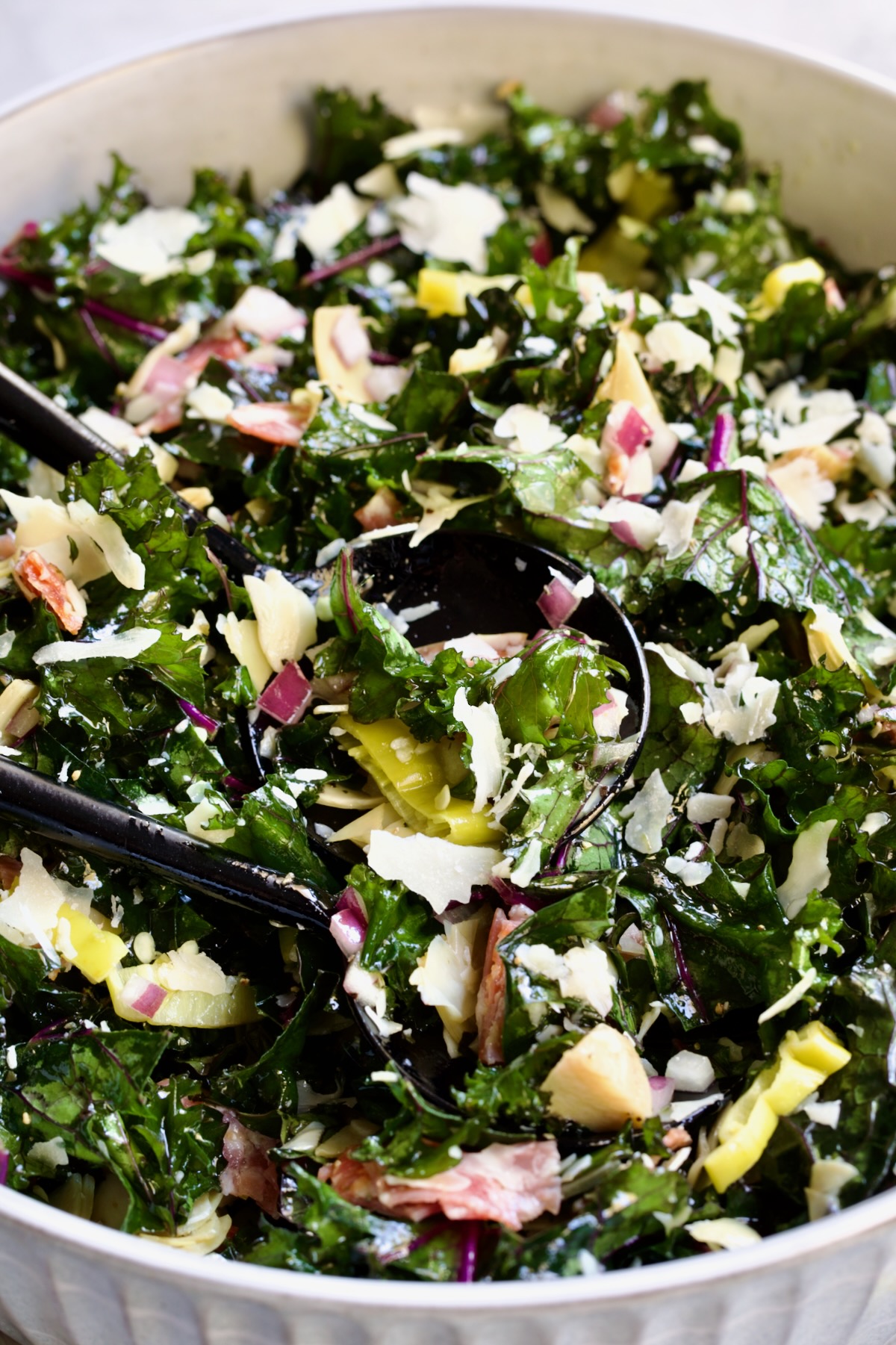 Chopped Kale Salad in round white bowl with black utensils scooping some up.