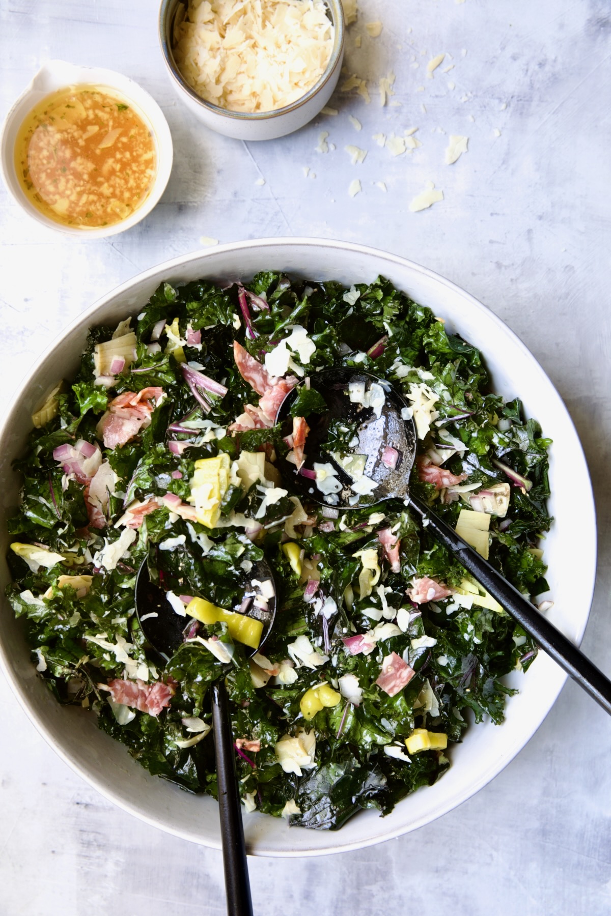 Chopped Kale Salad in round white bowl with black utensils scooping some up.