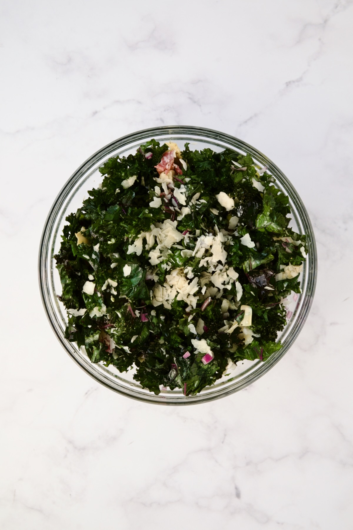 Ingredients for kale salad in glass bowl after being combined.