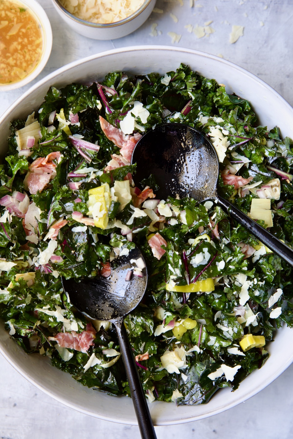 Chopped Kale Salad in round white bowl with black utensils.